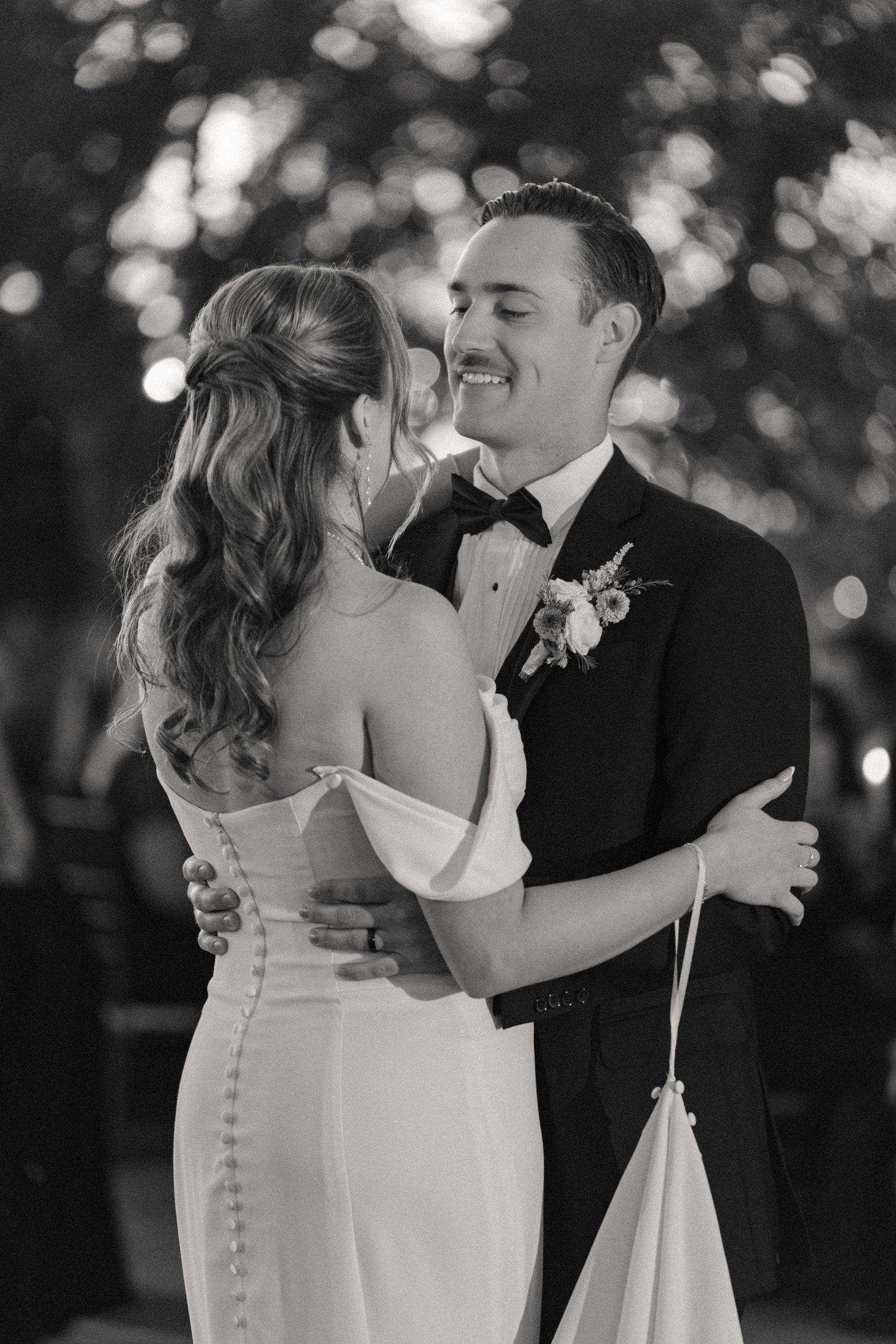 A romantic black and white portrait of newlyweds sharing their first dance under evening lights.
