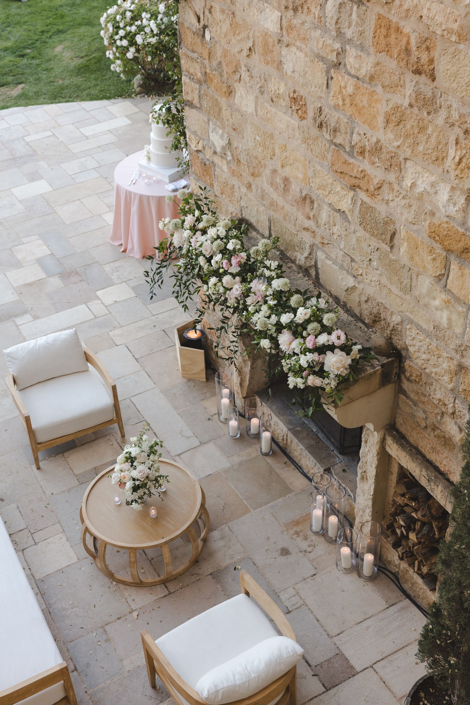 Cozy outdoor seating area decorated with white flowers and candles against a stone wall.