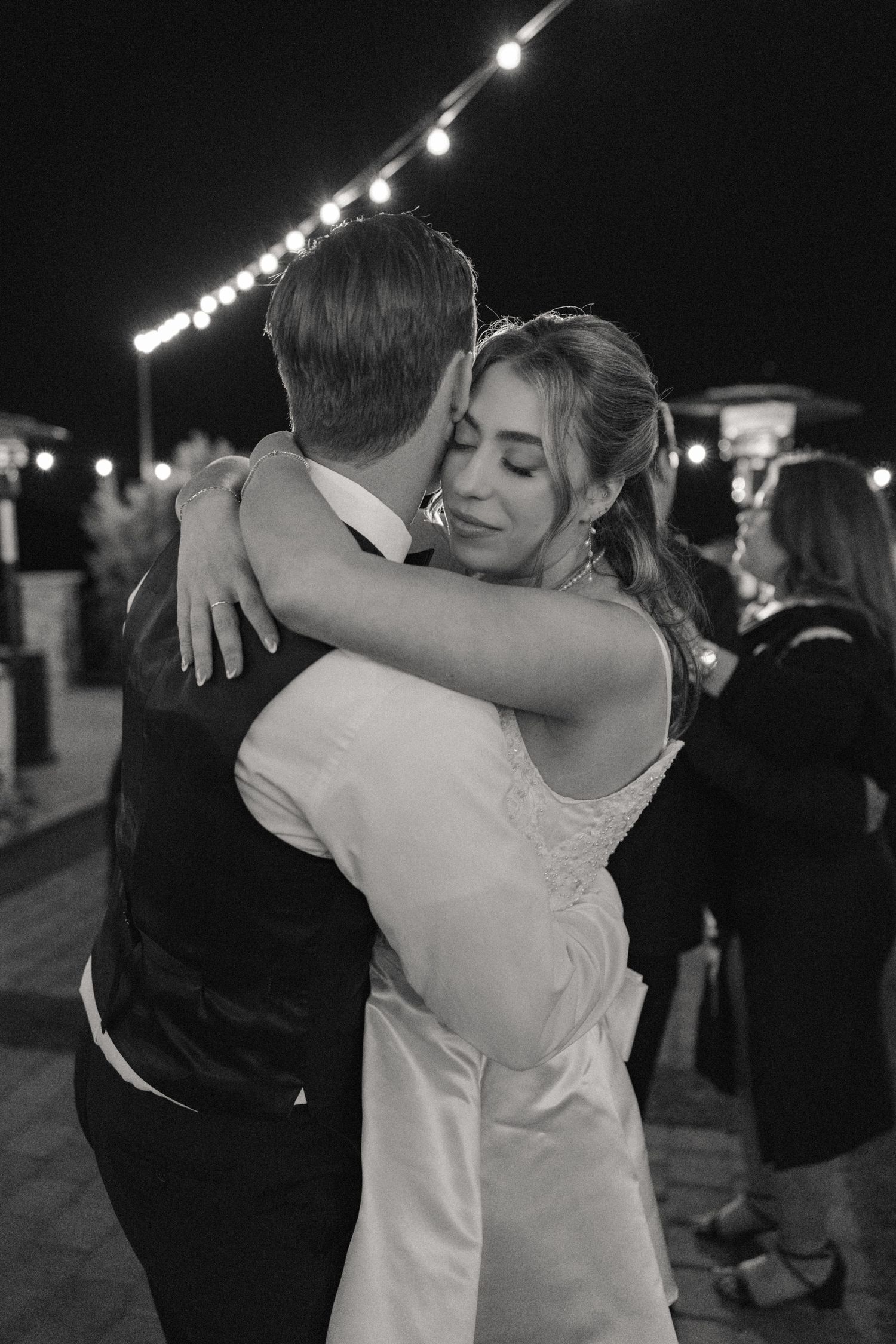 Couple dancing under string lights at nighttime wedding reception.