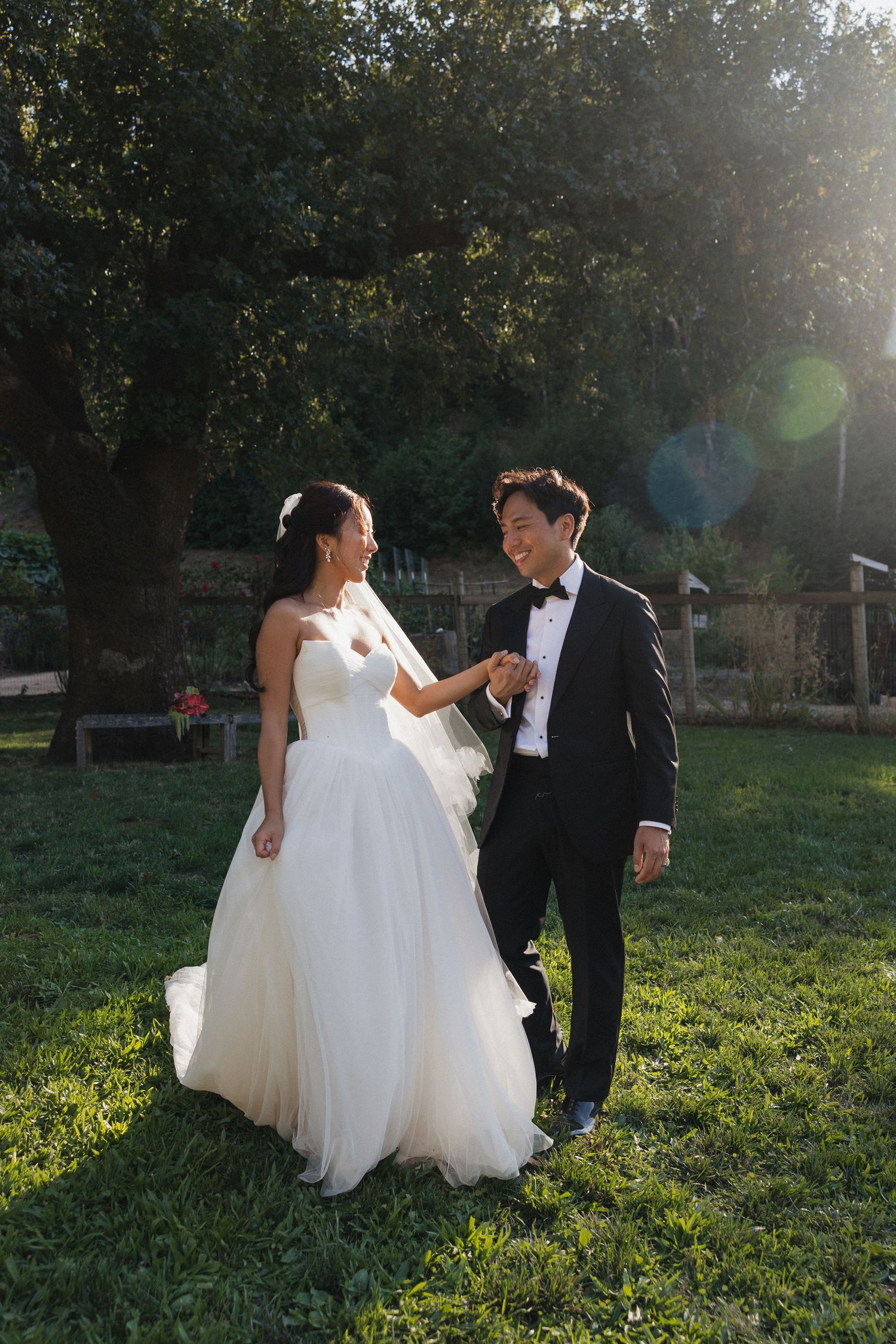 A bride and groom dance together on a sunlit lawn during their wedding day.