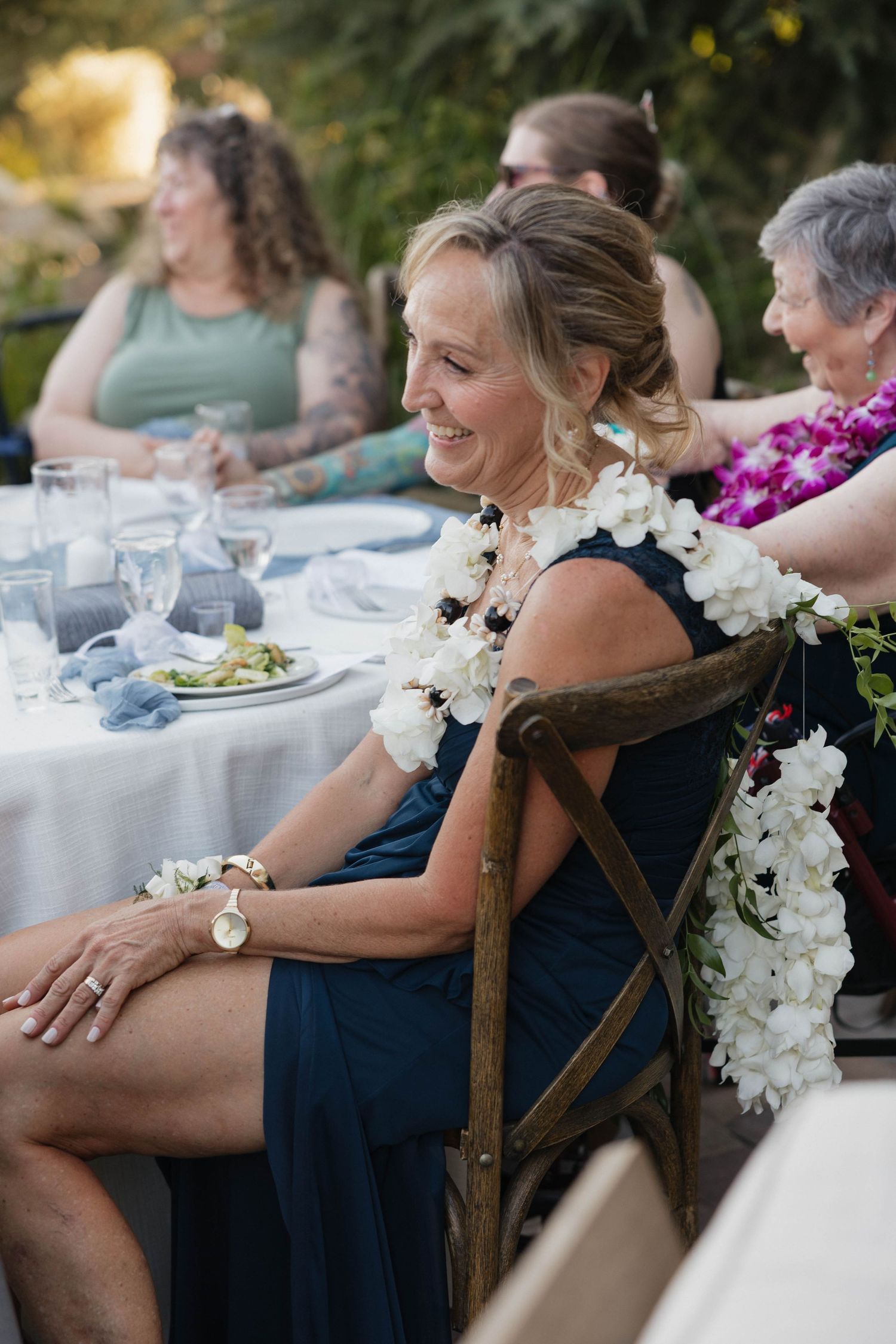 Wedding guests enjoying an outdoor reception dinner with white floral leis and table settings.
