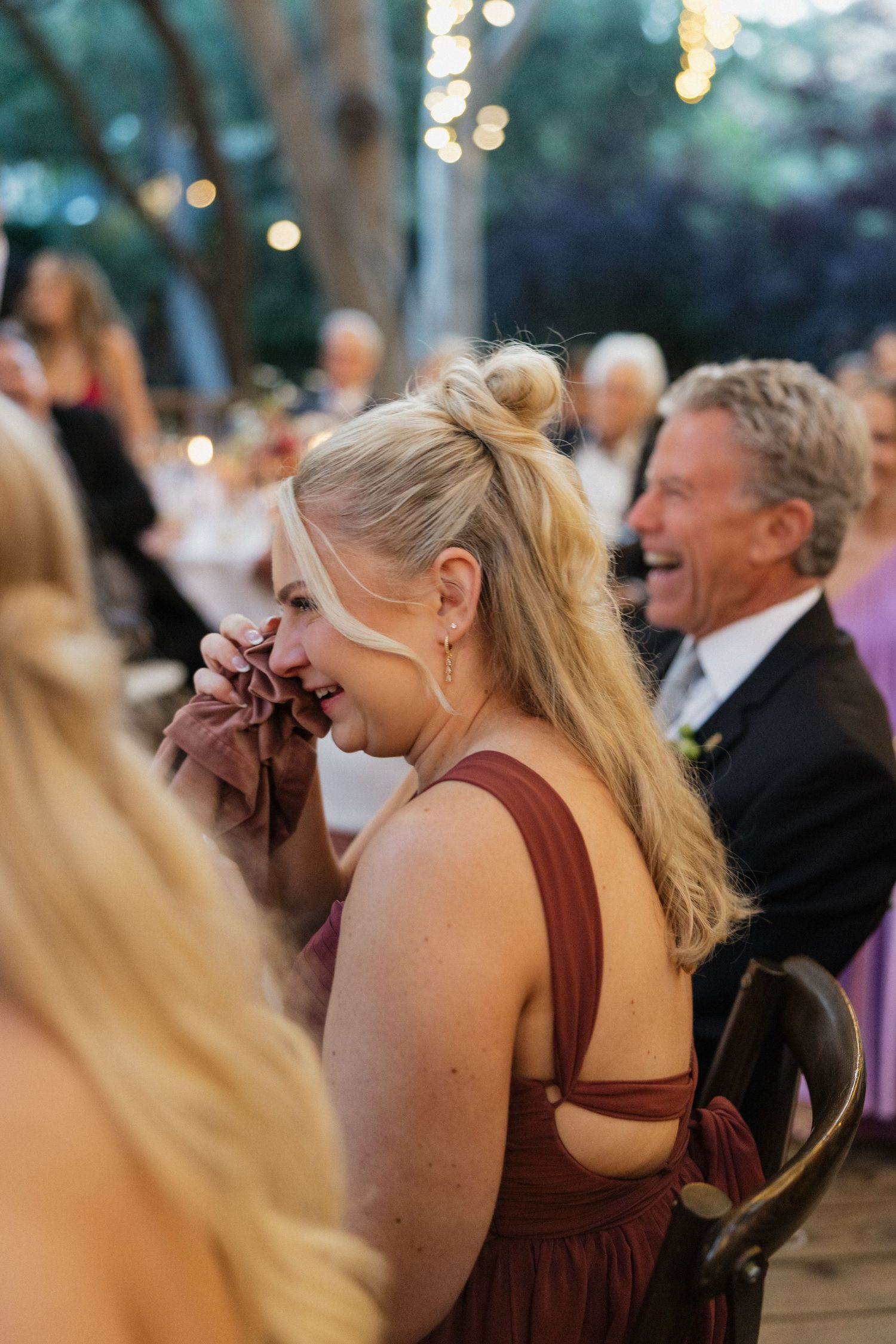 Emotional wedding guest in burgundy dress laughing and crying during speeches.