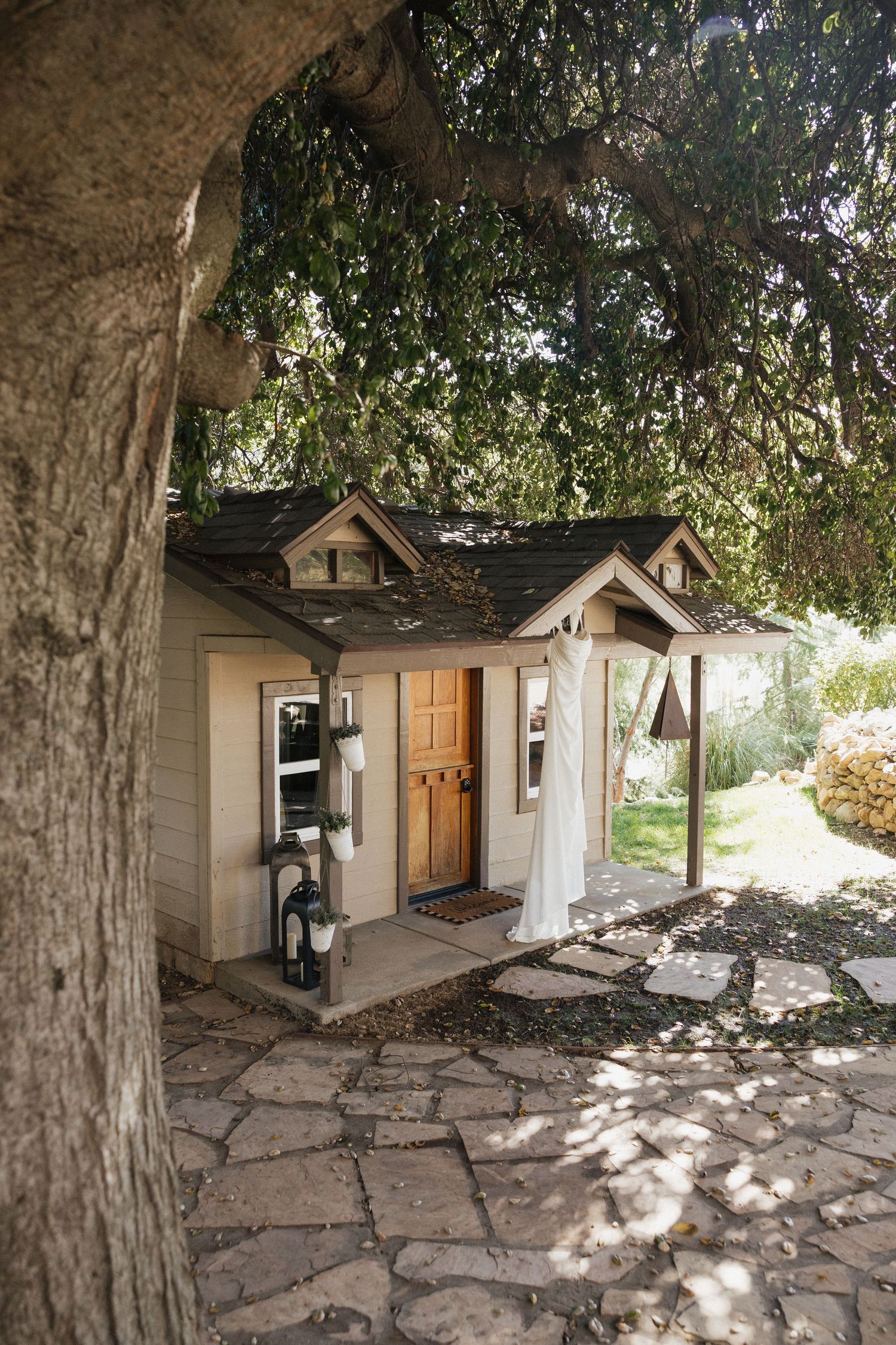 Small white cottage-style buildings with stone pathways and trees creating dappled shadows in natural lighting.