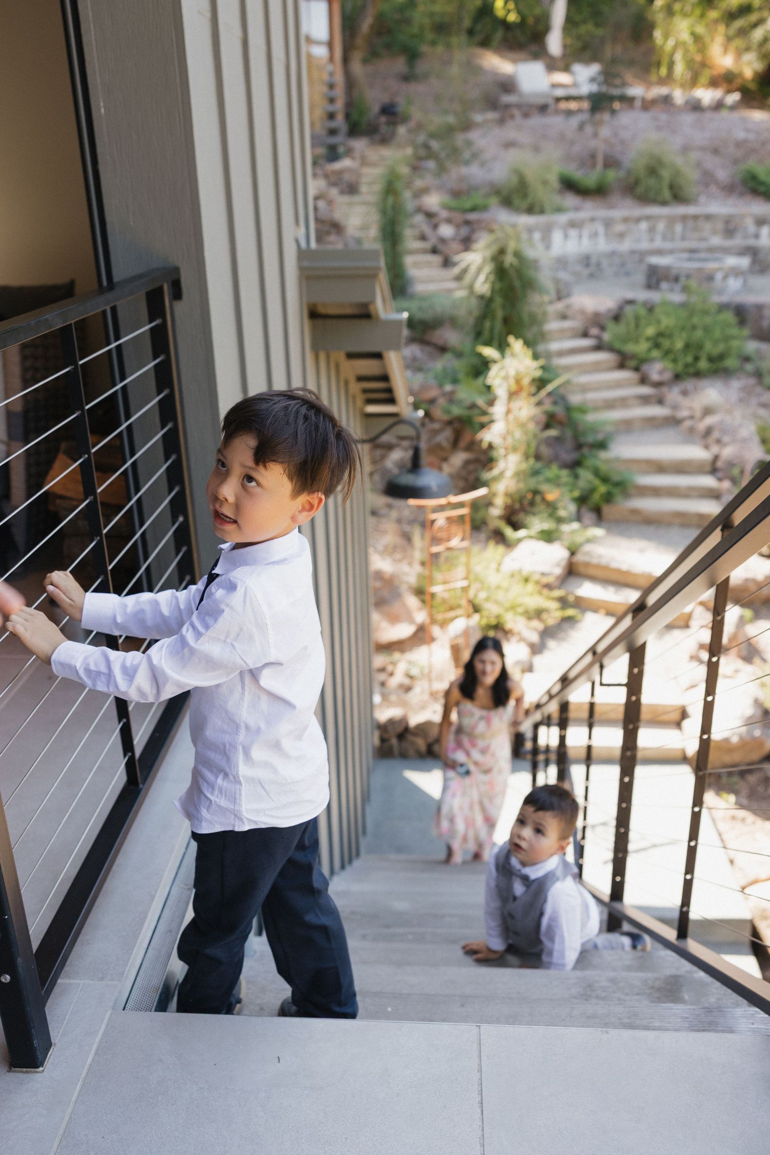 Child in formal attire playing on outdoor stairs with scenic mountain backdrop.