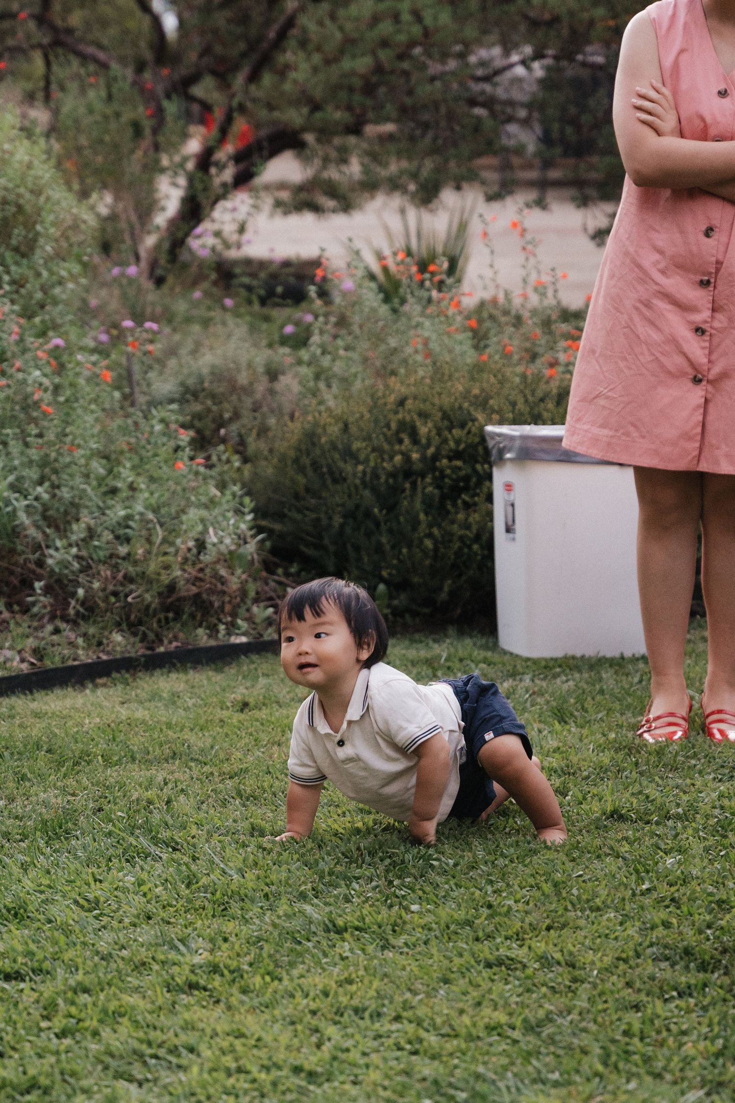 Small child crawling and playing on grass in outdoor garden setting.