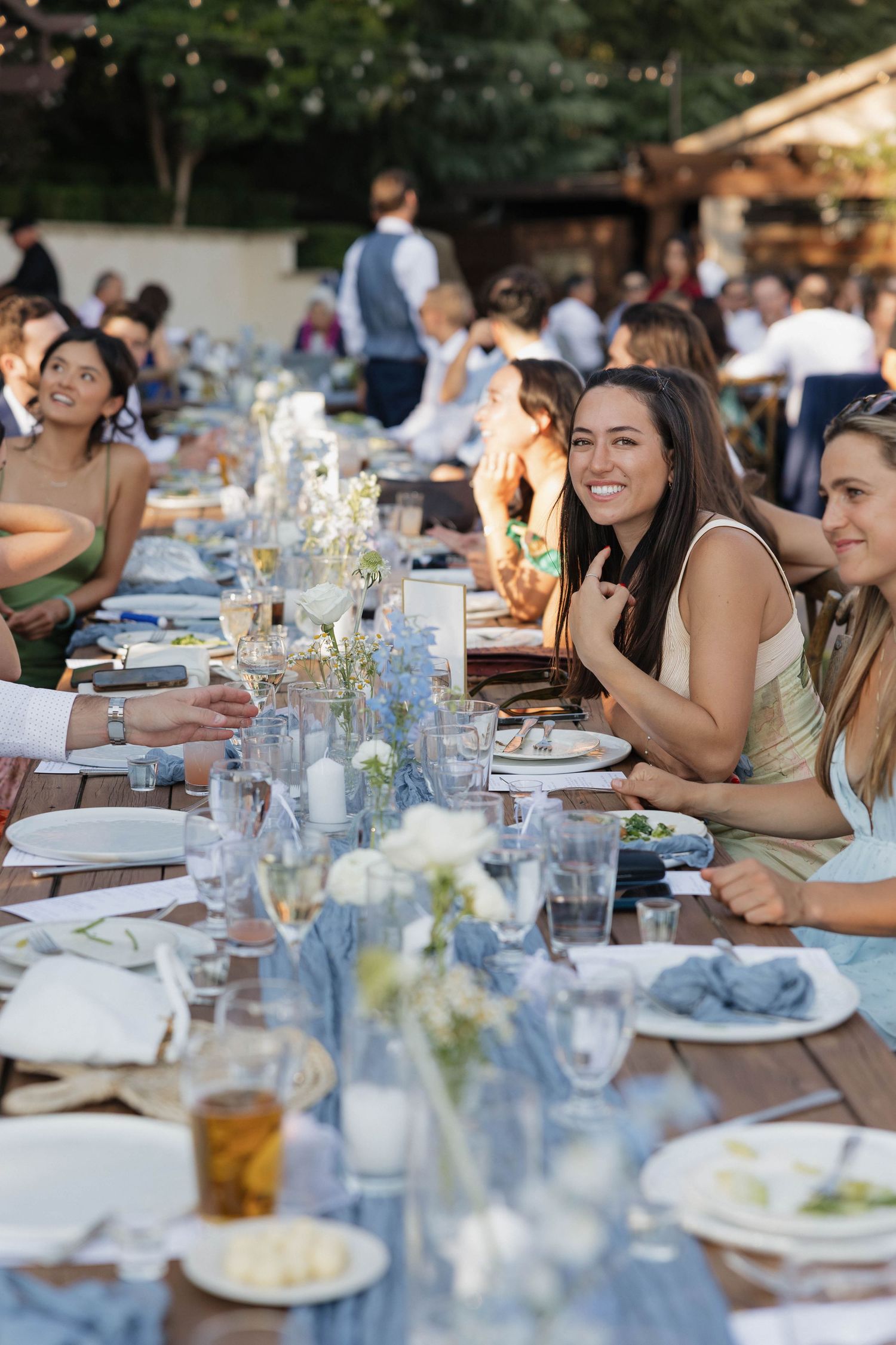 Long dining table set outdoors with elegant place settings and glassware for an alfresco gathering at sunset.