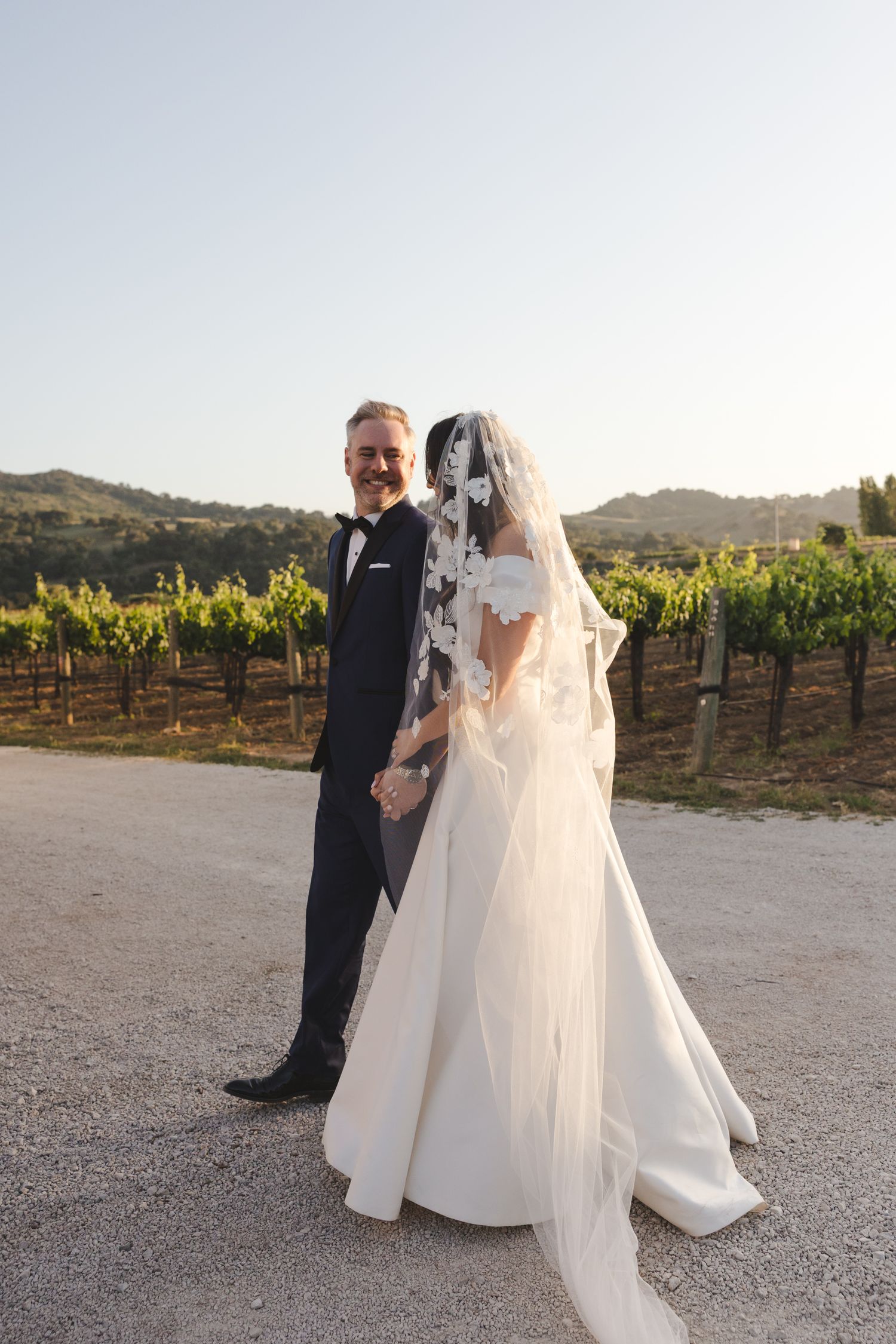 Elegant wedding portrait on pathway through wine country with rolling hills in background.