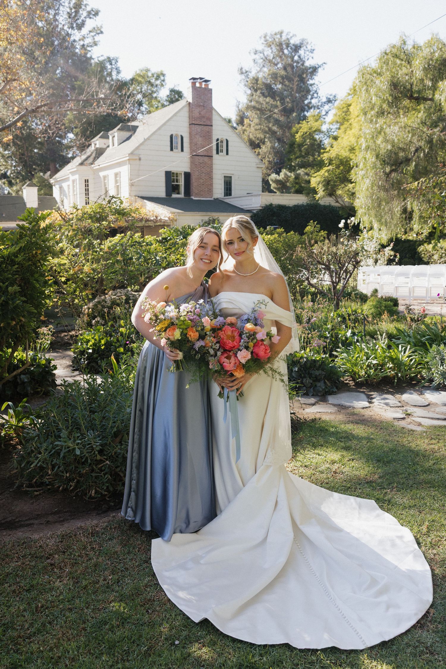 Bridal party in blue dresses holds colorful bouquets while posing in a garden setting.