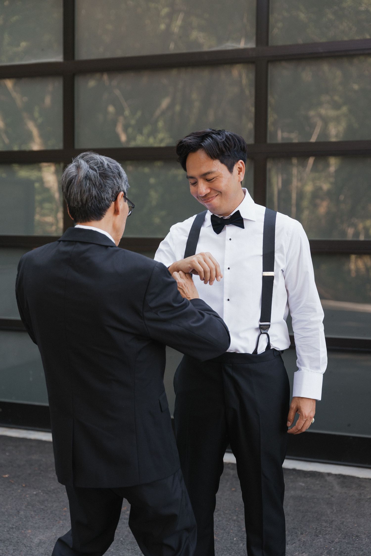 Two people in formal attire share a playful moment wearing black and white outfits with suspenders.