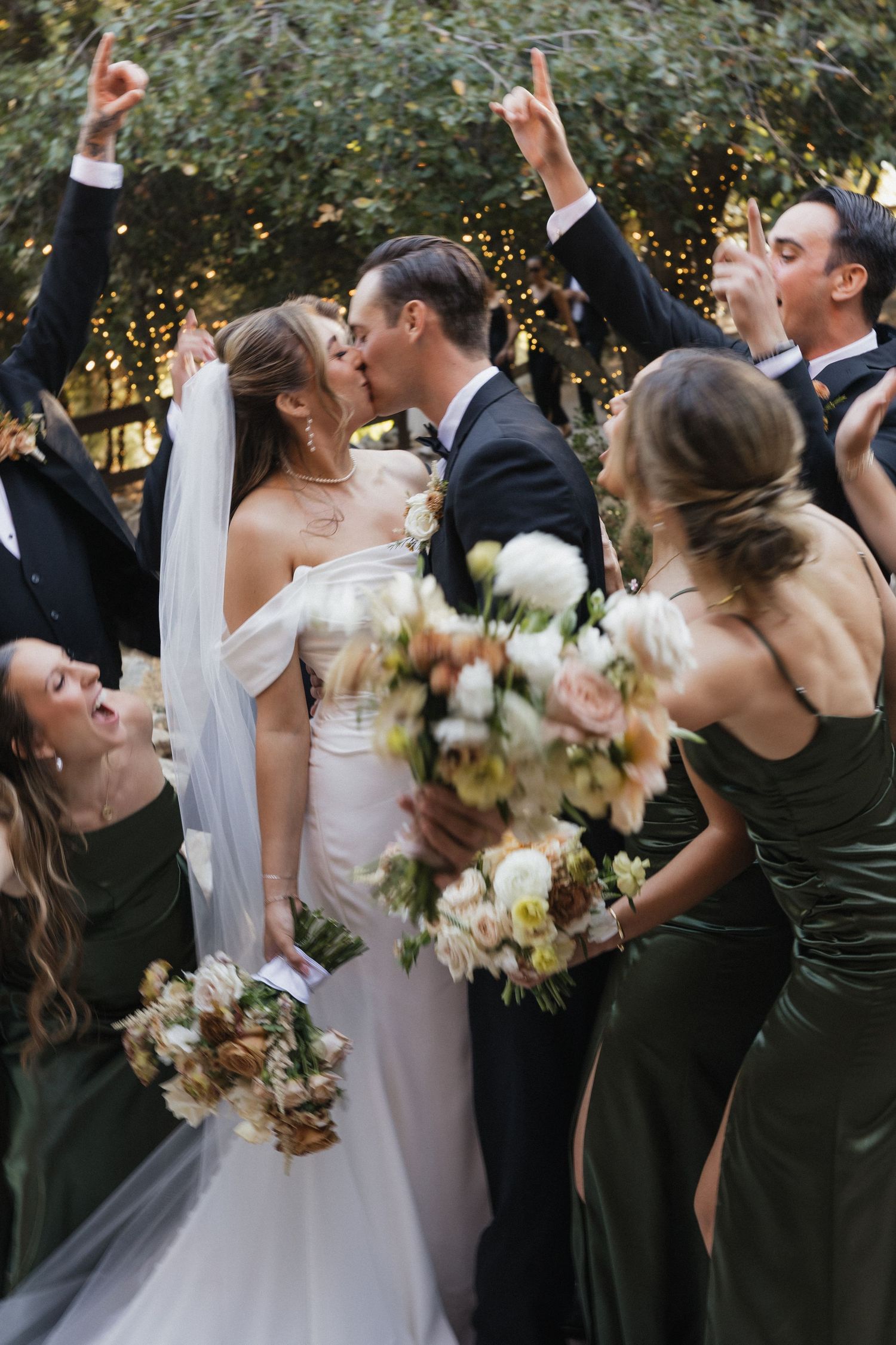 Wedding party in dark dresses and formal attire holding bouquets outdoors.
