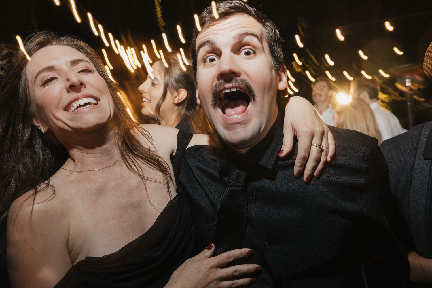 Wedding celebration with guests laughing under warm string lights.