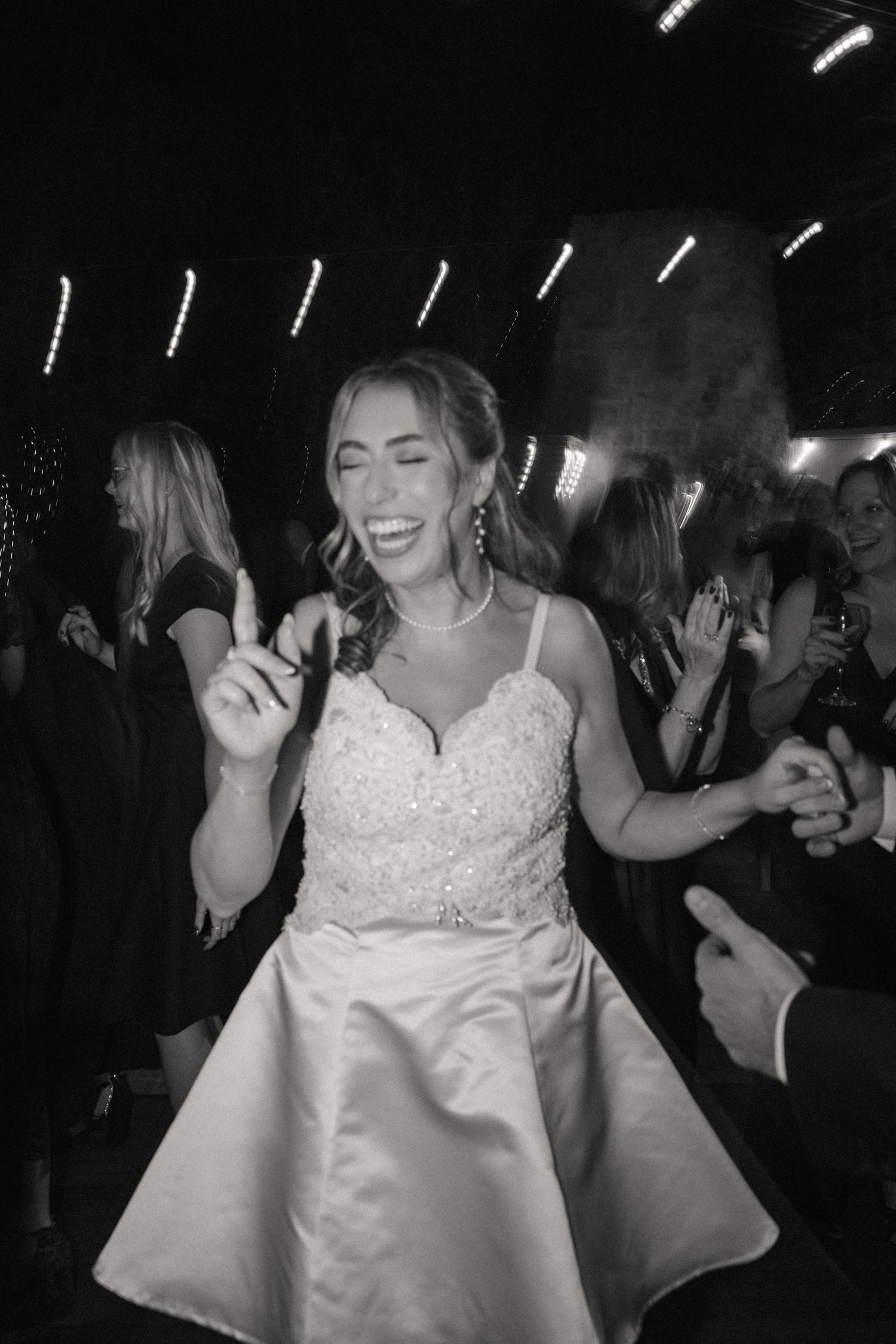 Wedding celebration with guests dancing and bride in white dress under evening lighting.