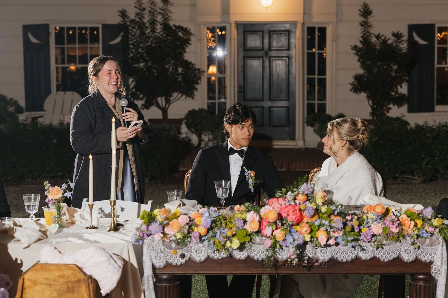 Wedding reception tables decorated with vibrant floral centerpieces and glowing candles under outdoor lighting.