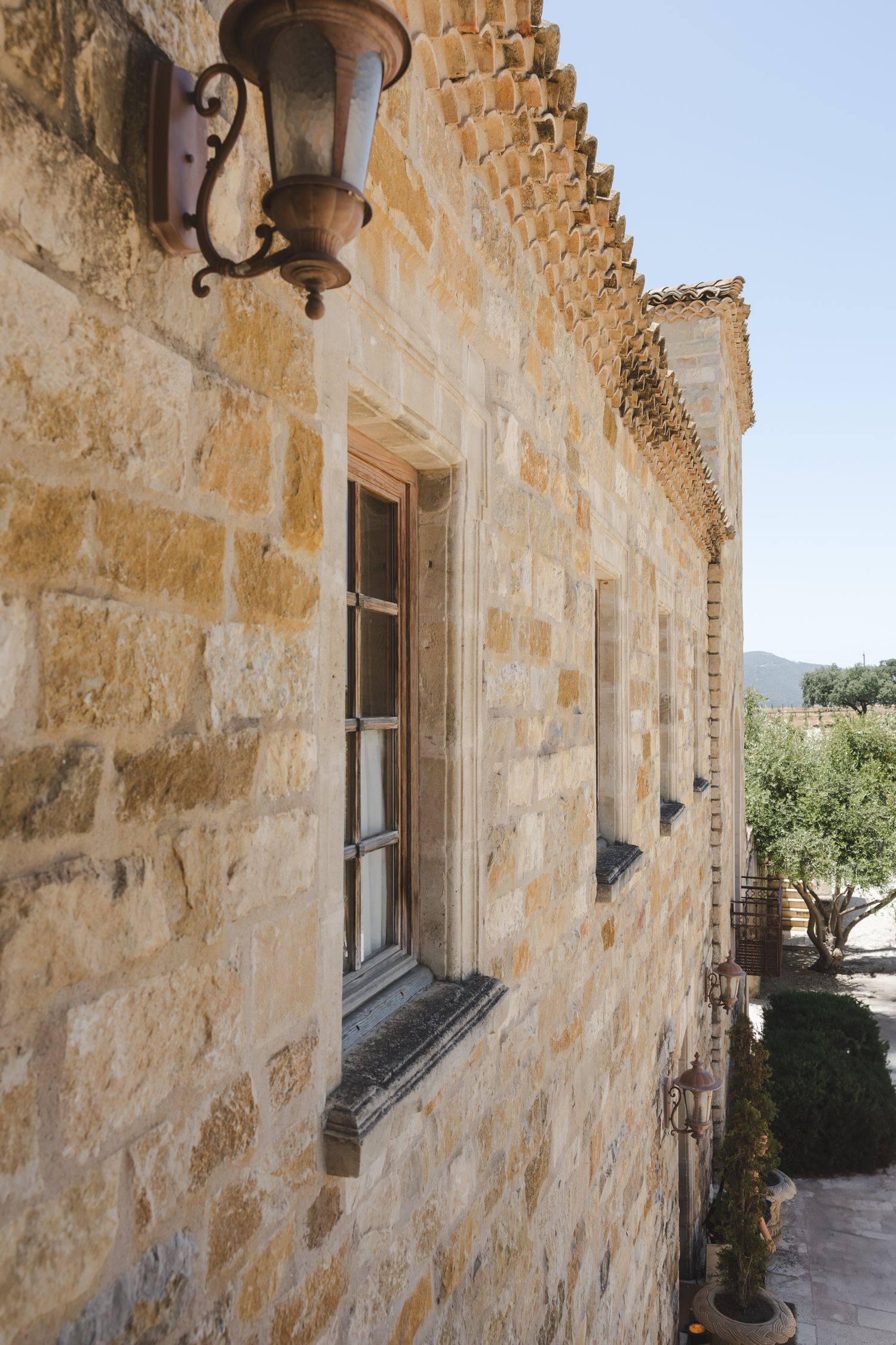 Ancient stone building exterior with rustic window and hanging lantern in Mediterranean architectural style.