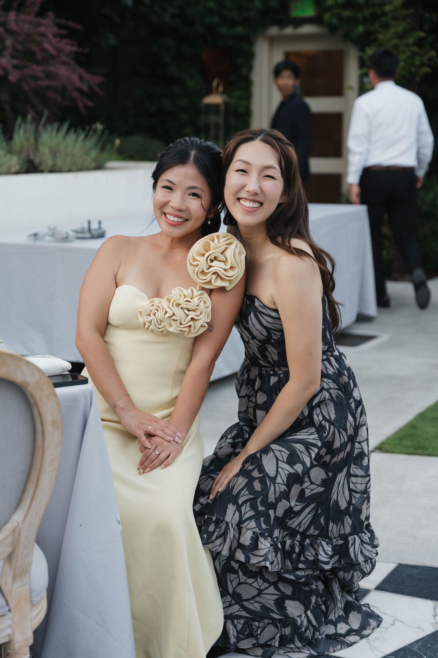 Two women in formal dresses pose together at an outdoor event.