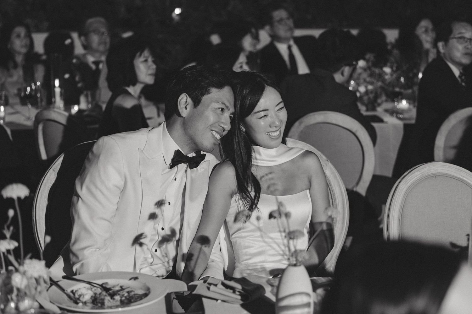 Wedding reception guests seated at elegant dining tables in evening setting.