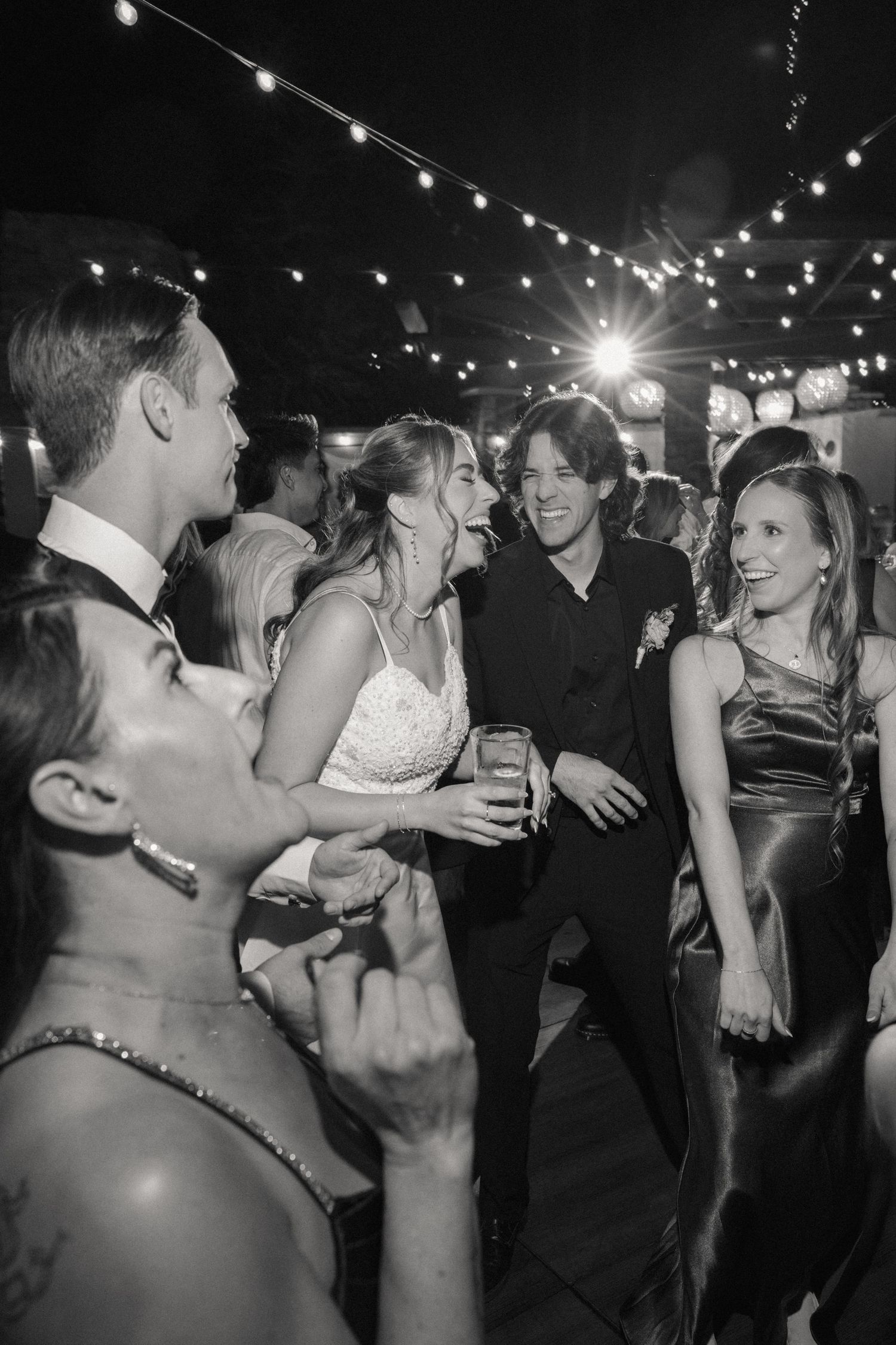 Wedding reception dance party with string lights overhead creating festive atmosphere.