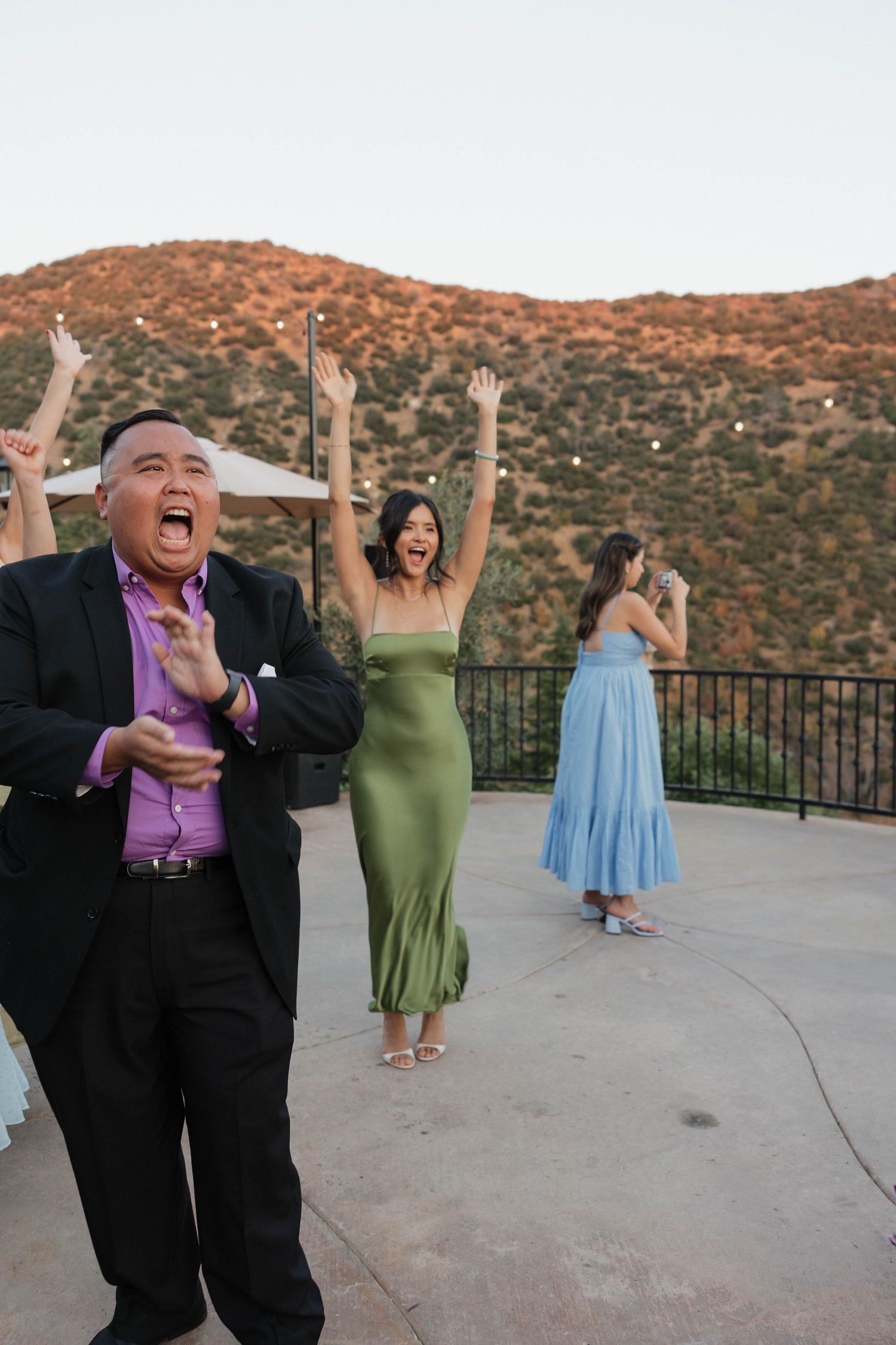 Joyful wedding celebration with guests dancing on outdoor patio with mountain views.