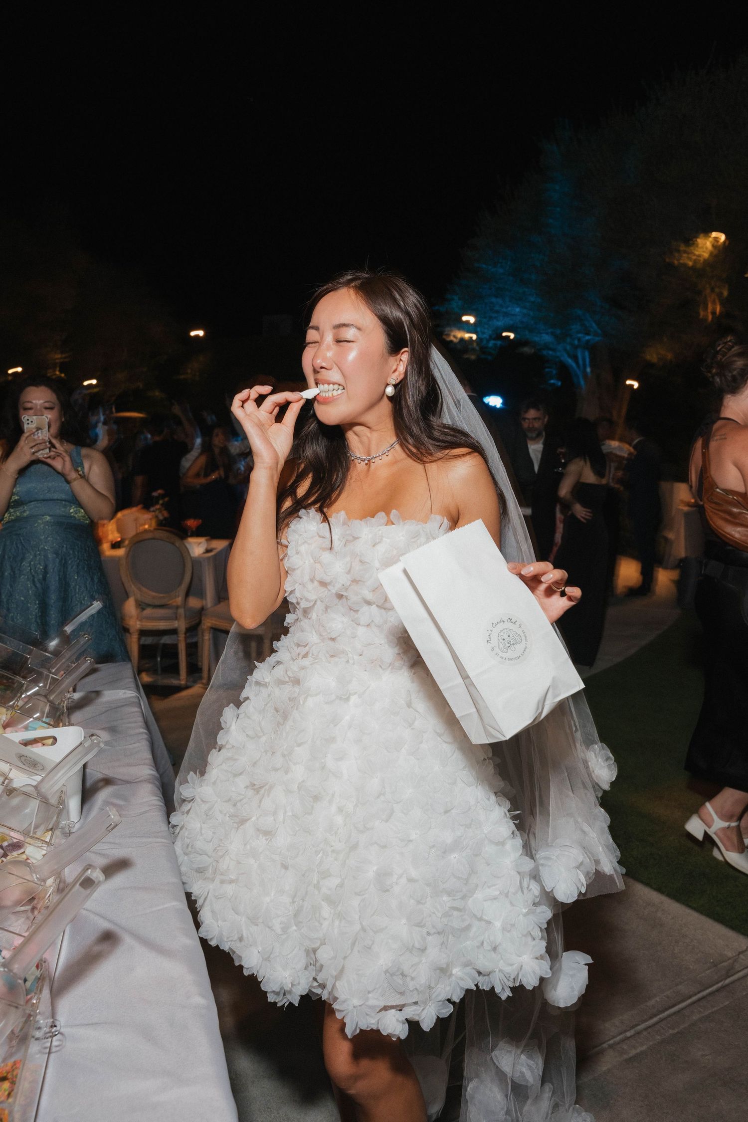 A bride in a white ruffled dress enjoys festivities at an outdoor evening celebration.