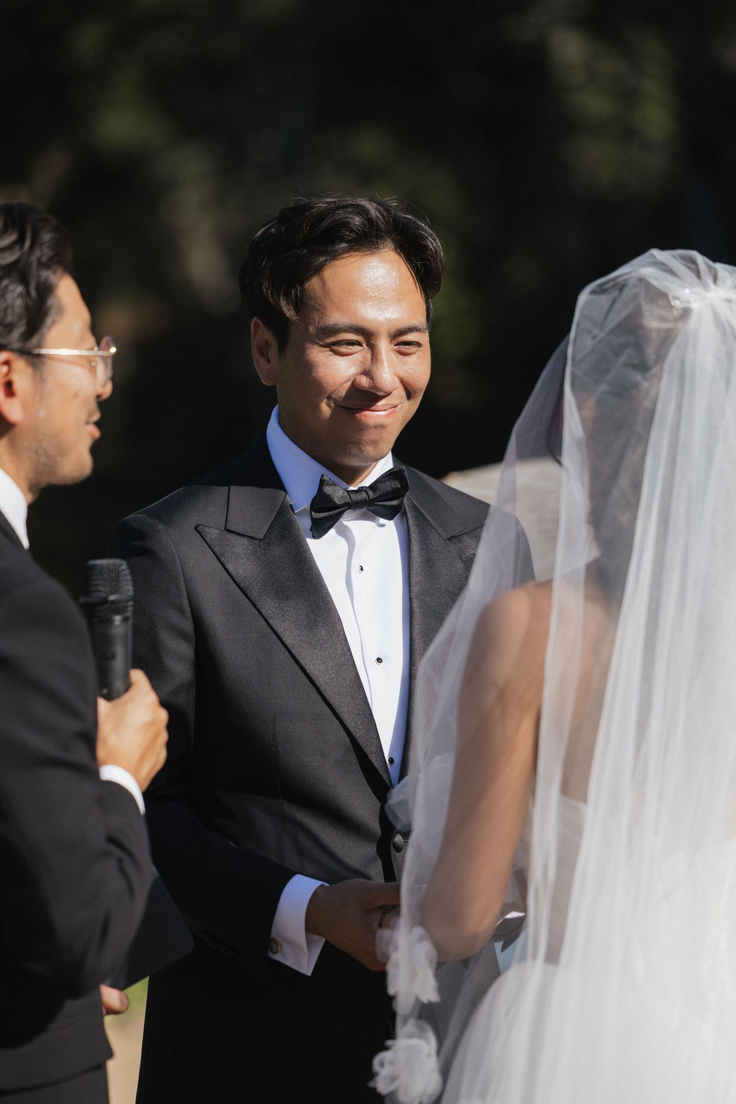 A wedding ceremony moment captured with flowing white veil in natural outdoor lighting.