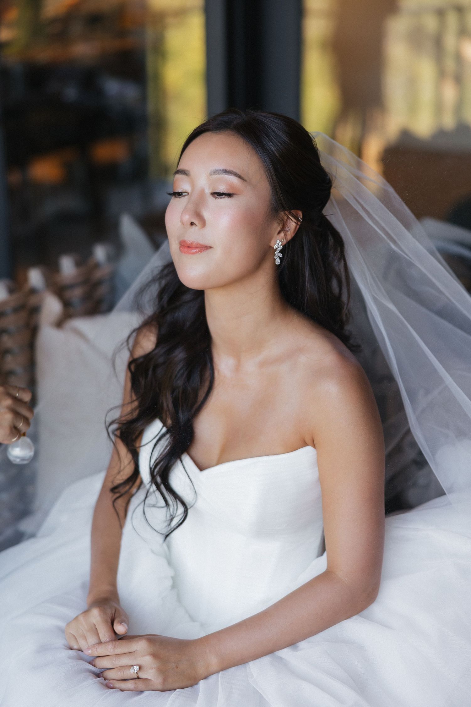 A bride in a strapless white wedding dress and veil poses with closed eyes and serene expression.
