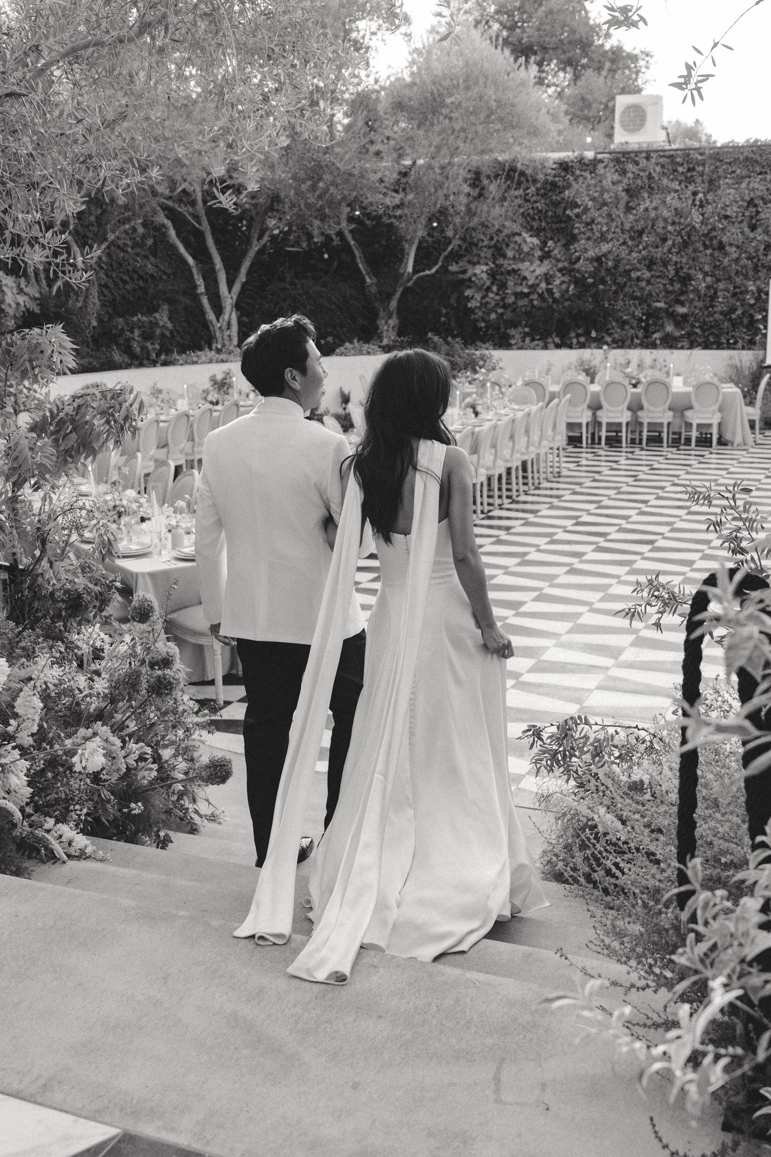 A couple overlooks their outdoor wedding venue with rows of chairs on a checkered floor.