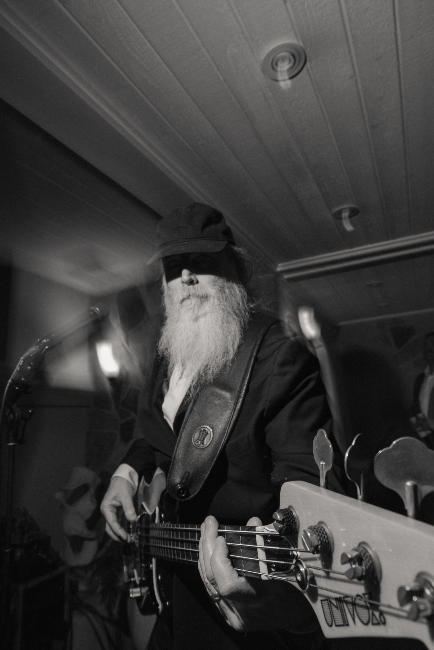Elderly bearded musician plays bass guitar on stage at a wedding reception in black and white.
