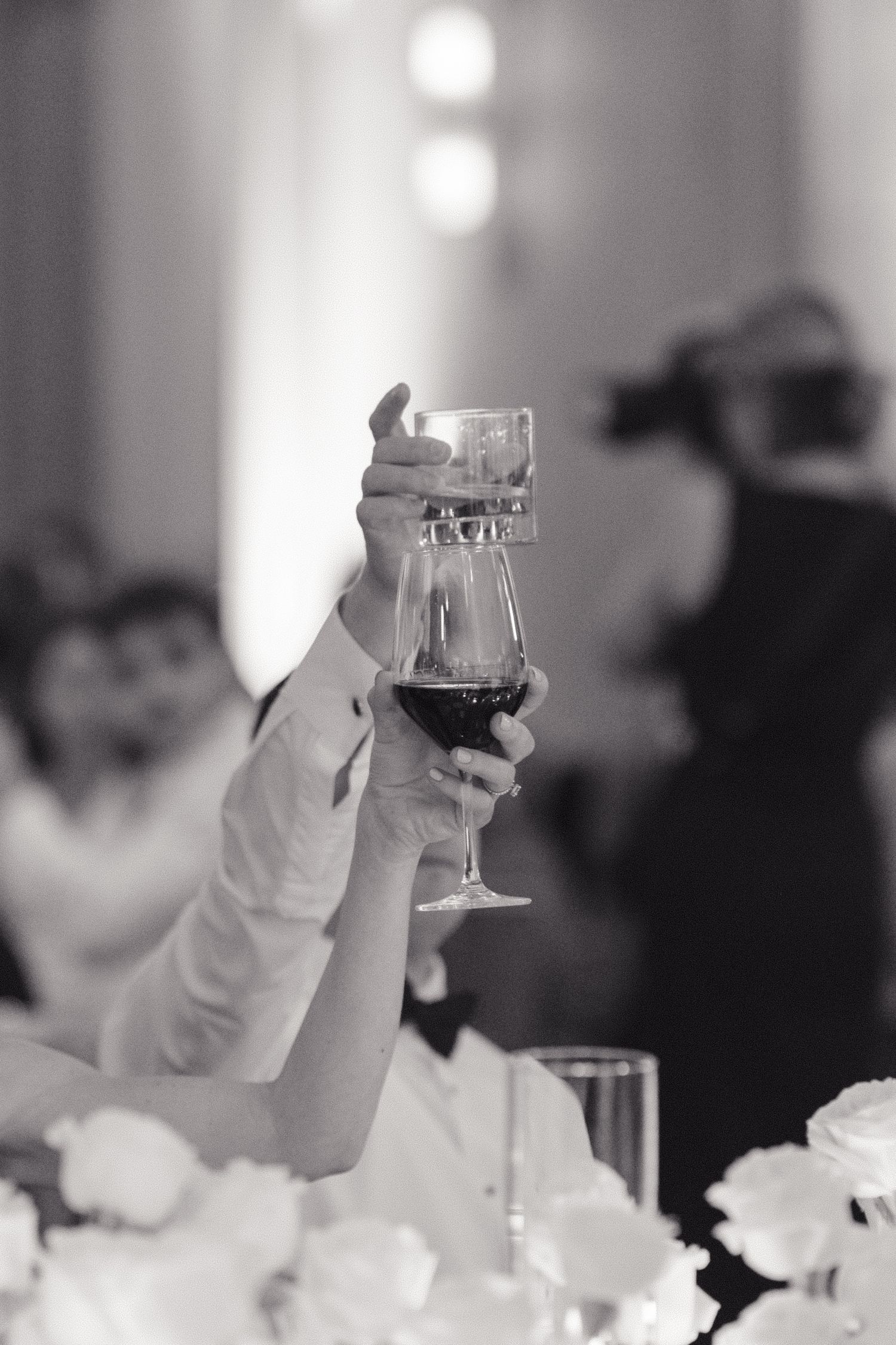 A hand raises a wine glass in celebration during an elegant black and white event with blurred background lighting.