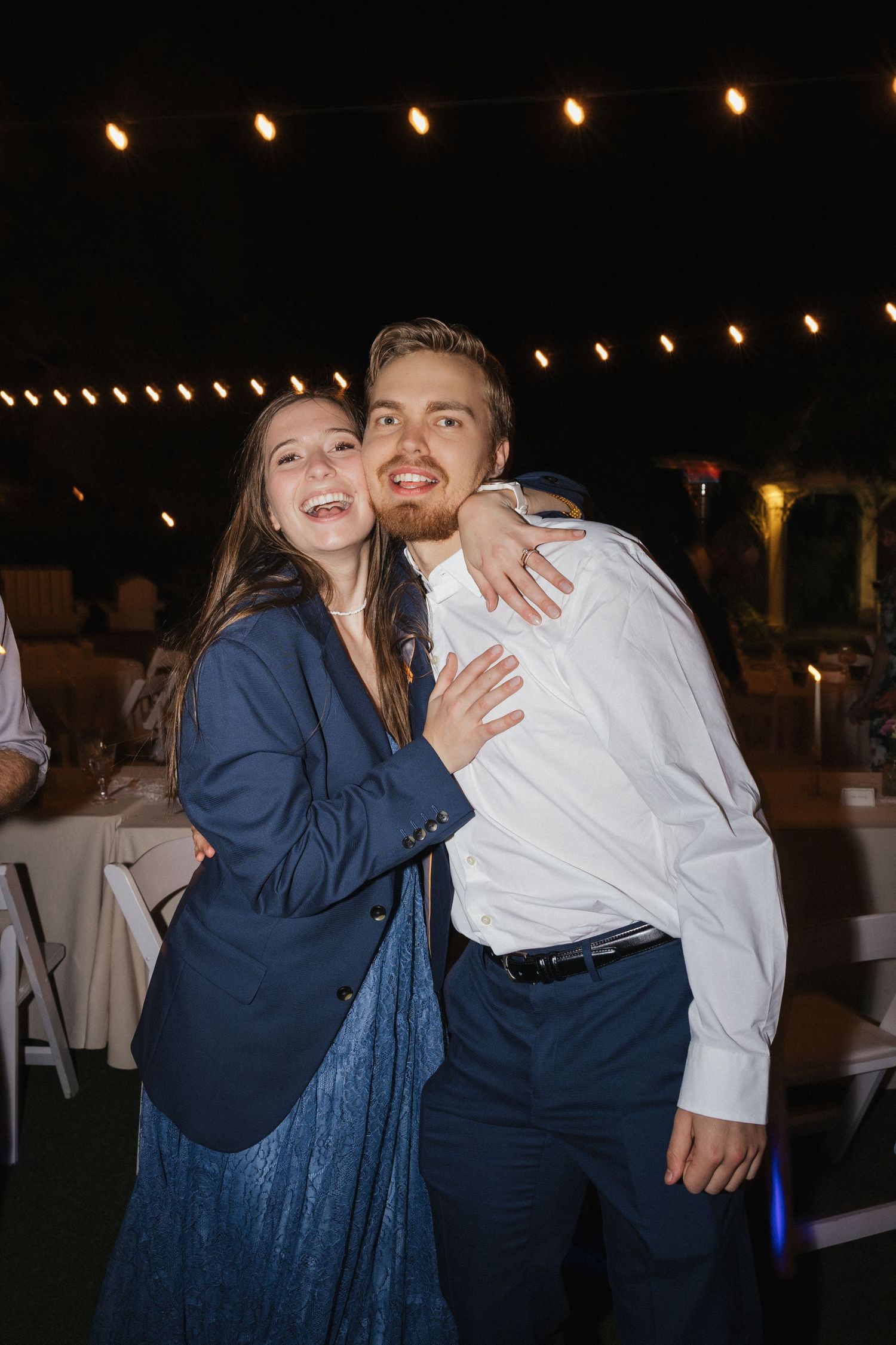 Wedding guests dancing and celebrating at outdoor reception under string lights.