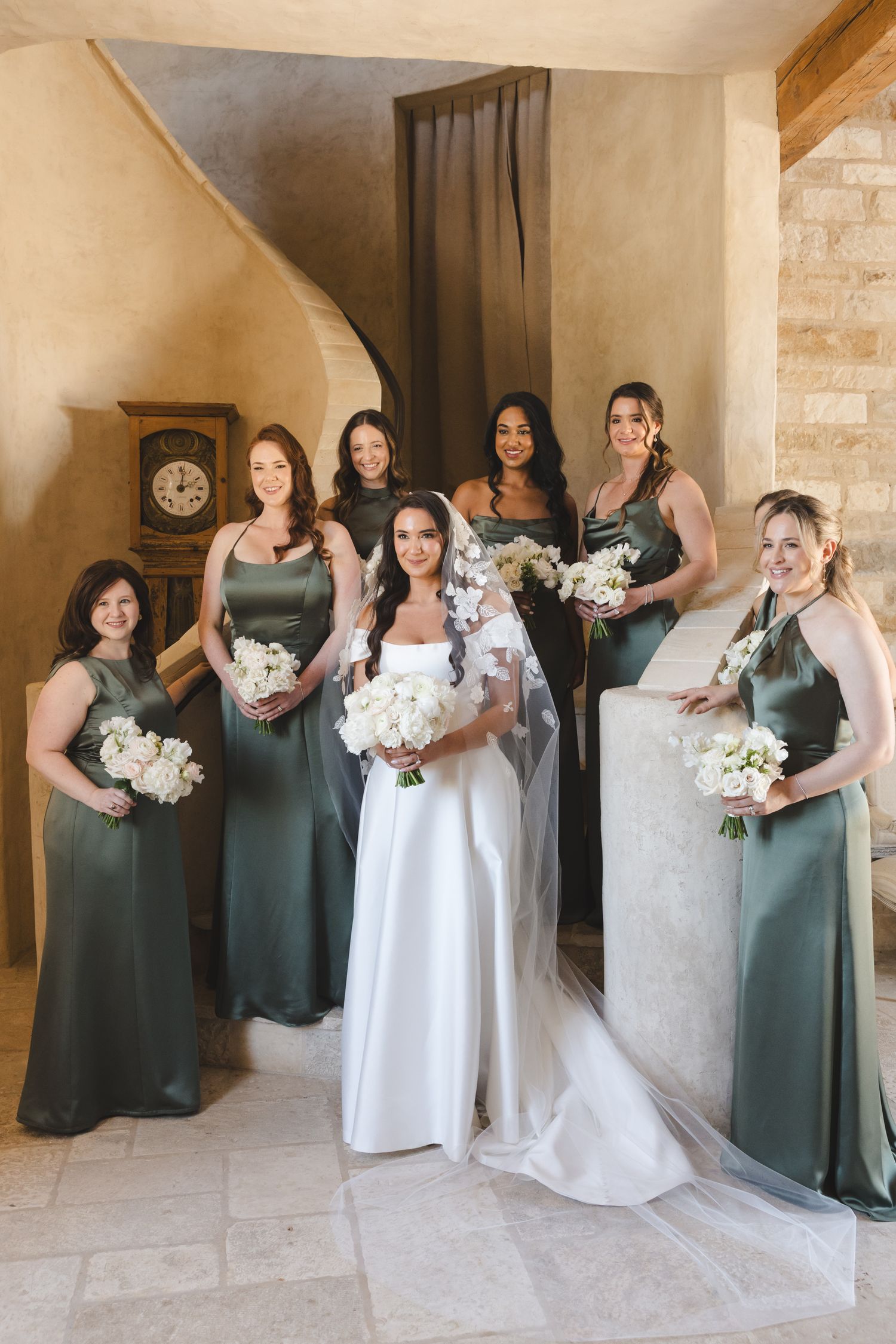 Wedding party with bridesmaids wearing sage green dresses posing in elegant indoor setting.