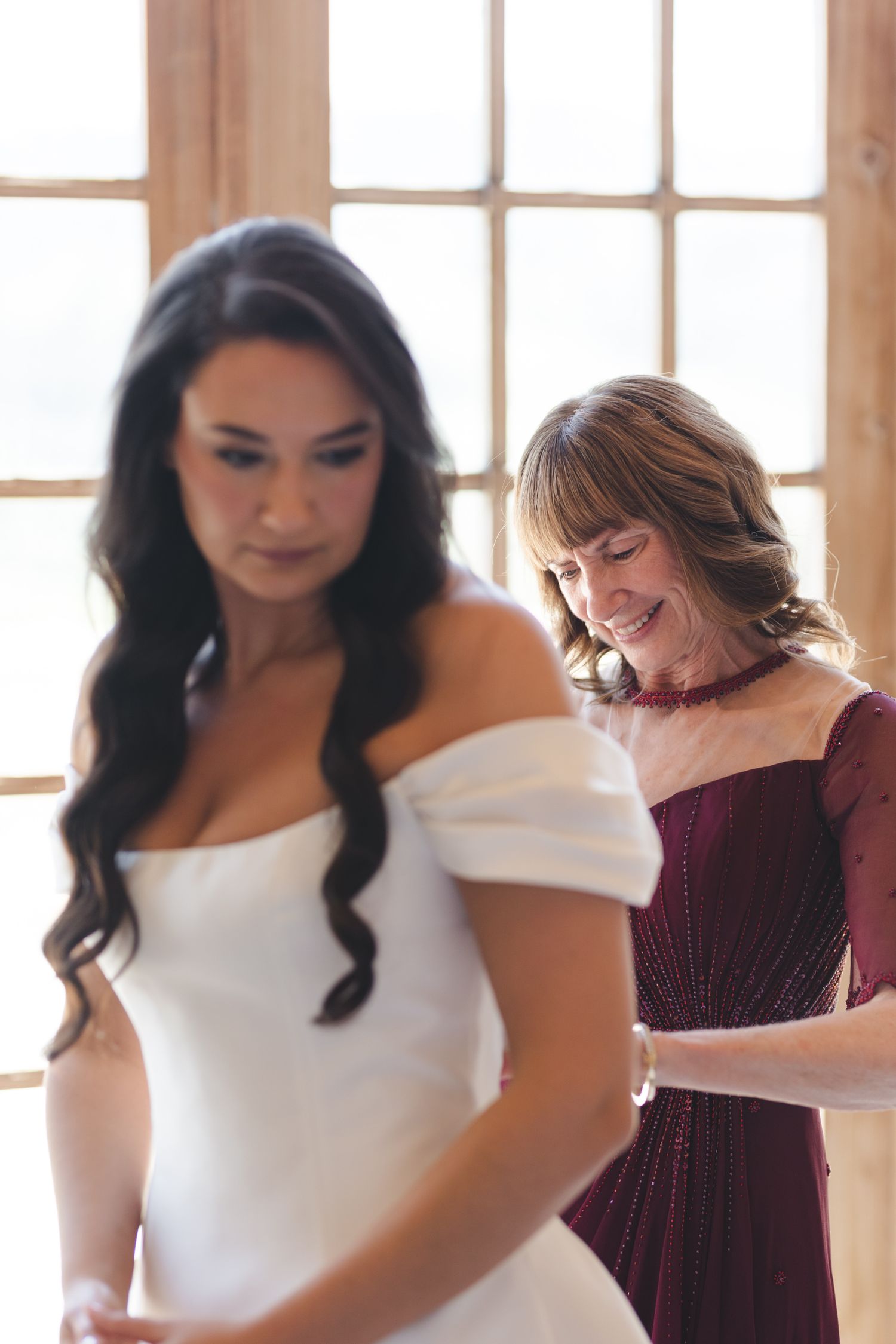 Elegant bridal party getting ready scene with mix of white and burgundy dresses in sunlit room.