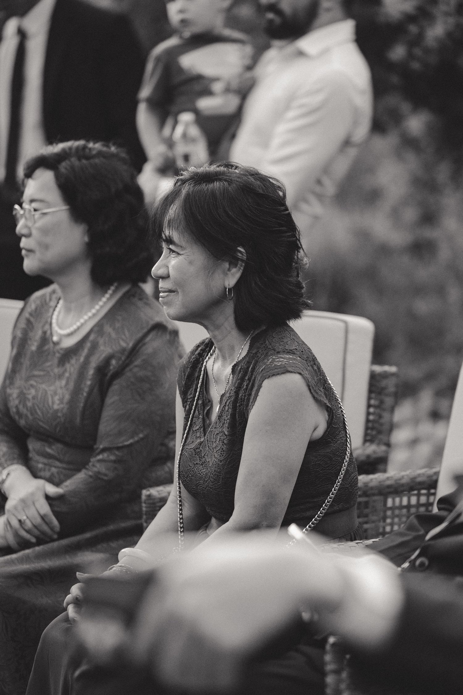 Two guests in elegant evening attire seated at an outdoor wedding ceremony.
