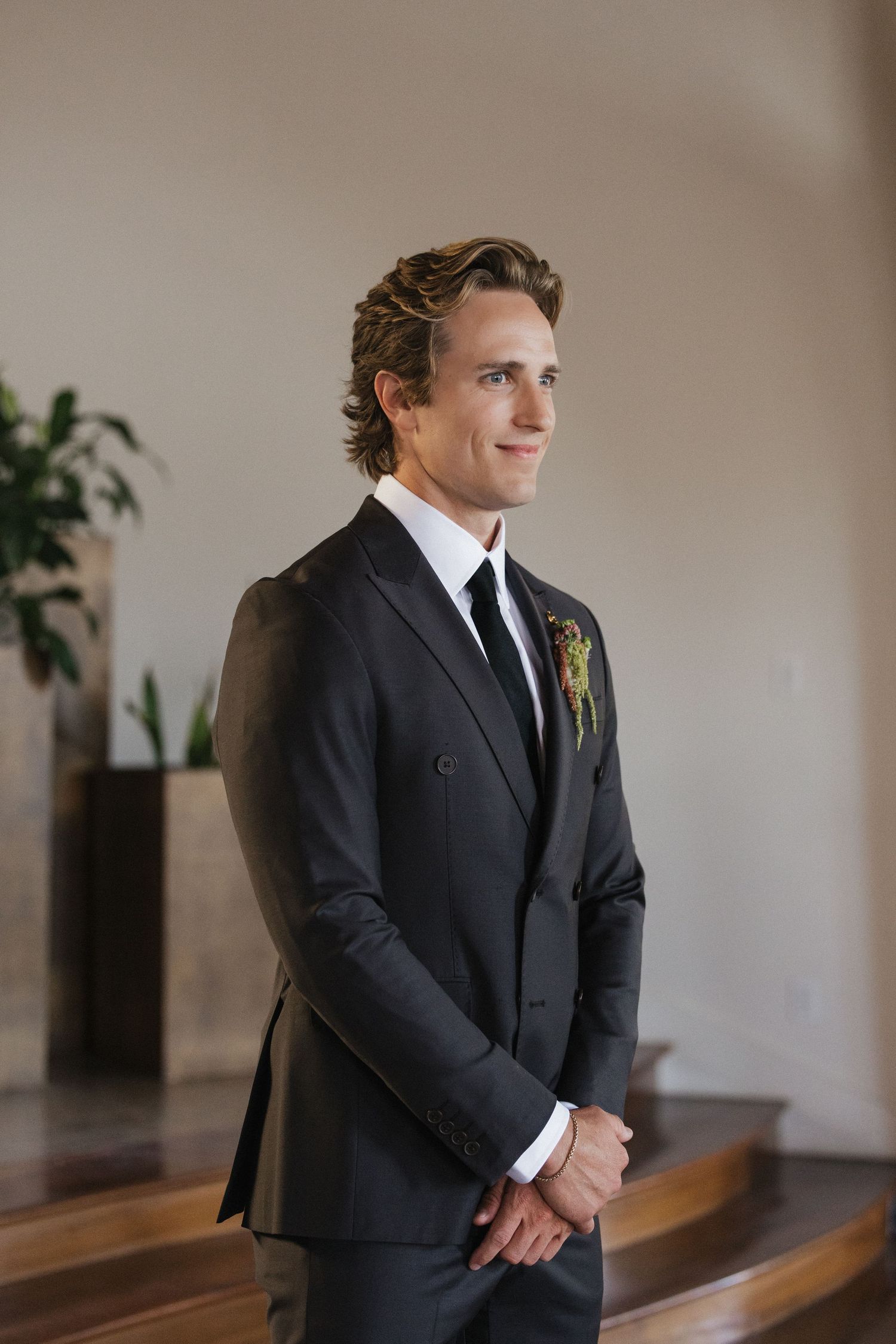 Groom in dark suit with boutonniere smiling at wedding ceremony.
