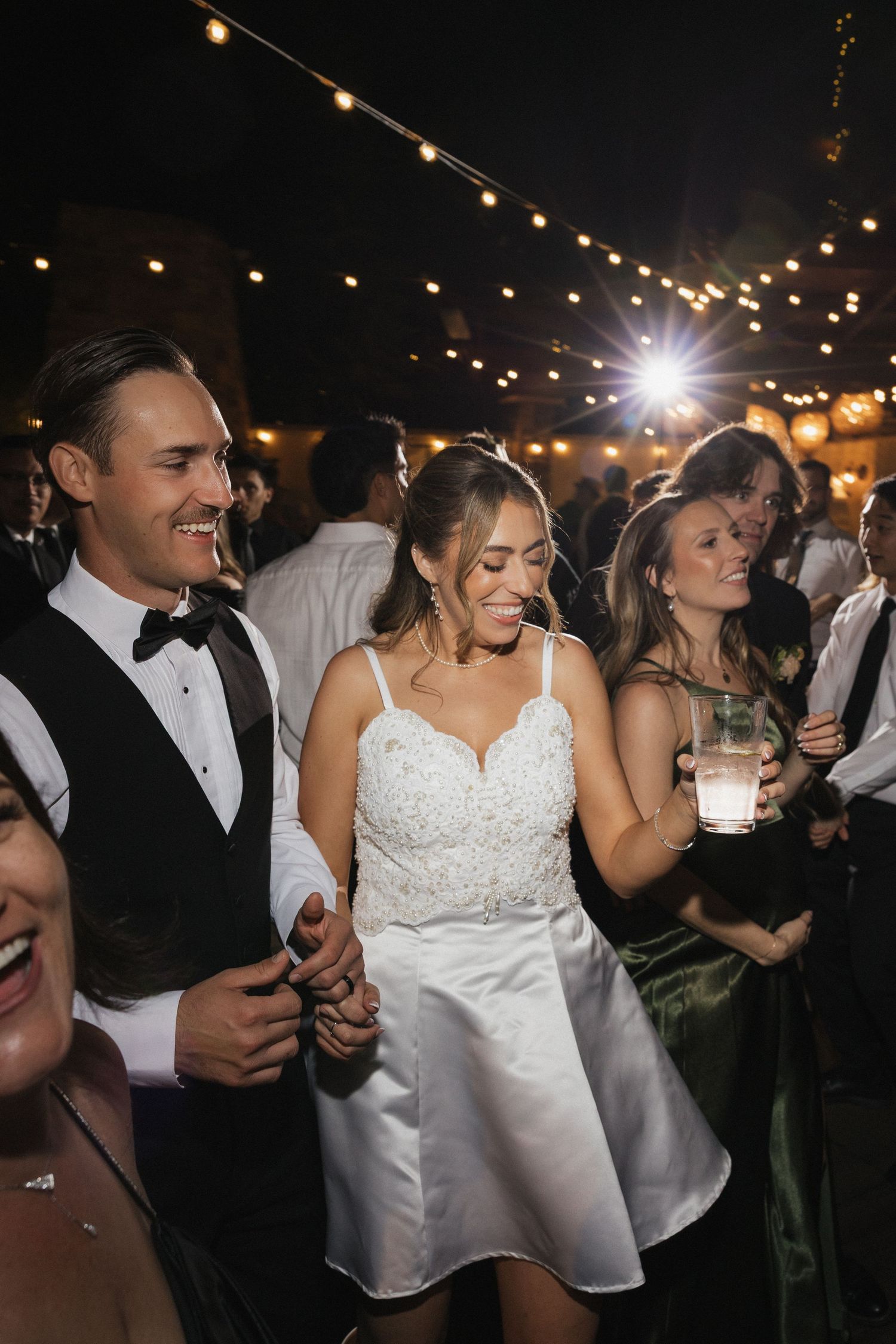 Wedding reception dance party under string lights at night.