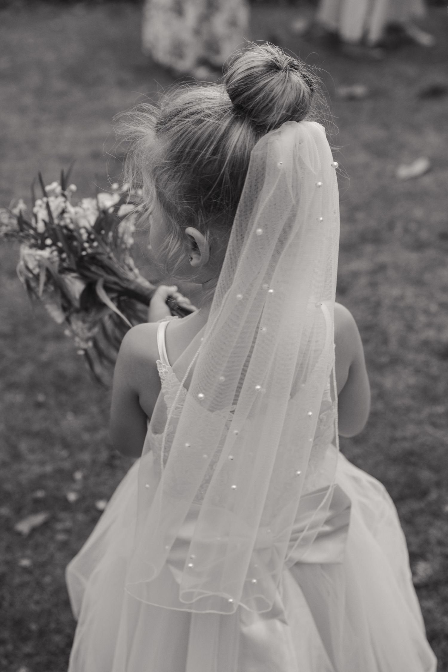 A child in a white dress and delicate pearl-dotted veil stands outdoors, shown in multiple similar angles.