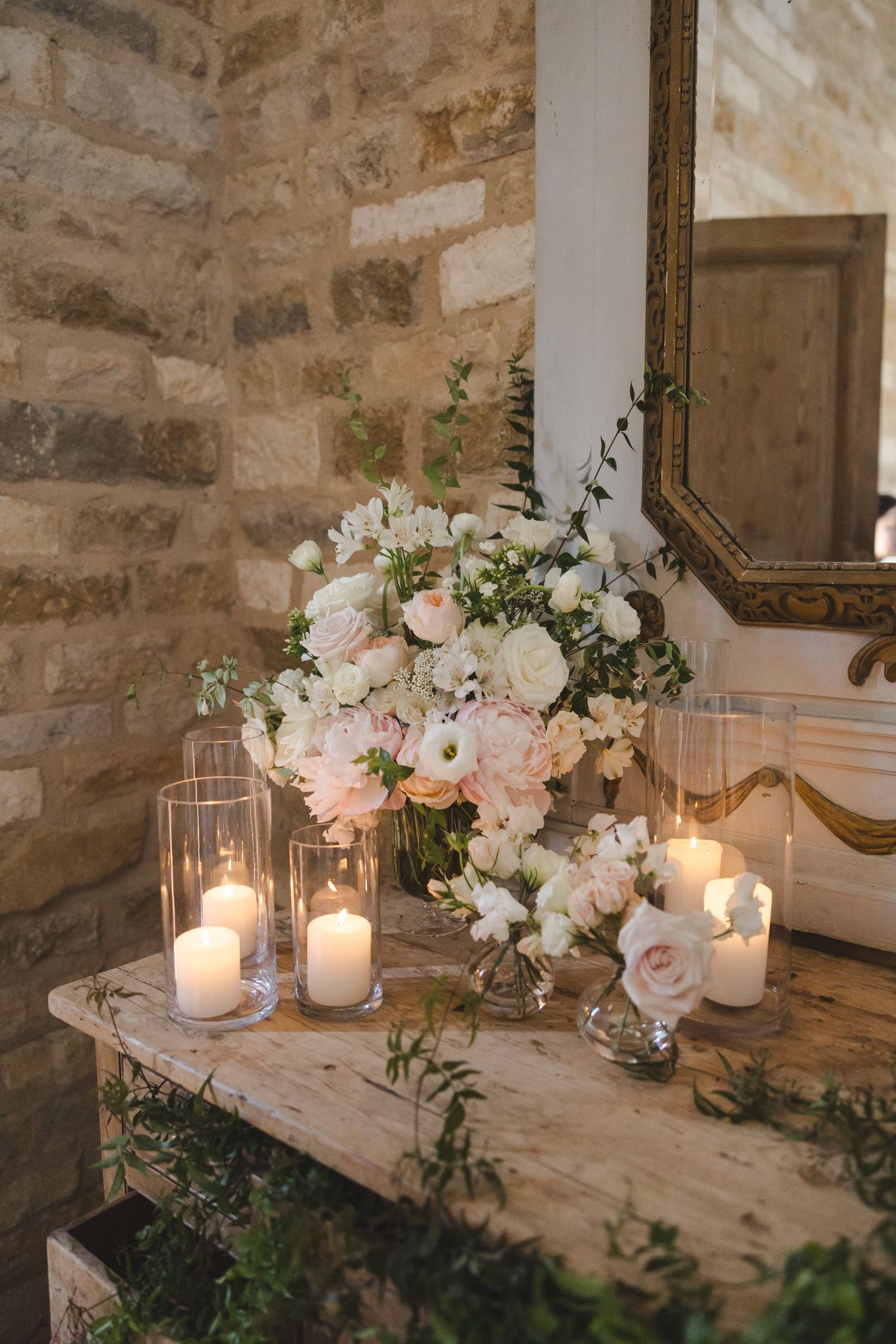 Romantic table setting with white floral arrangements and glowing candles against stone walls.
