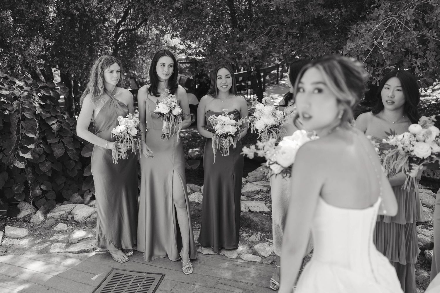 Wedding party poses outdoors in coordinated gray dresses with white floral bouquets.