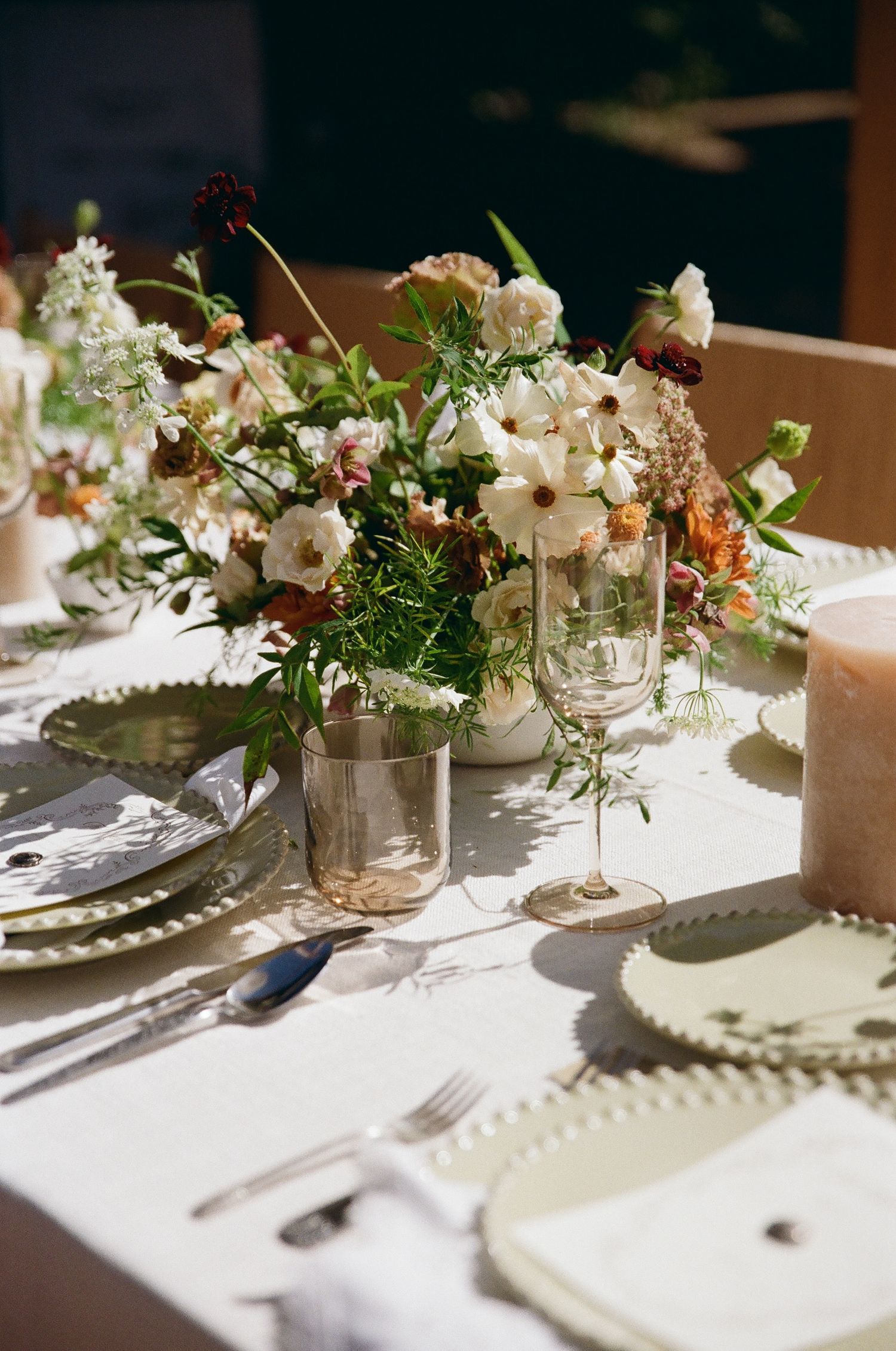 Elegant table settings with white floral centerpieces in mason jars casting soft shadows across white tablecloths.