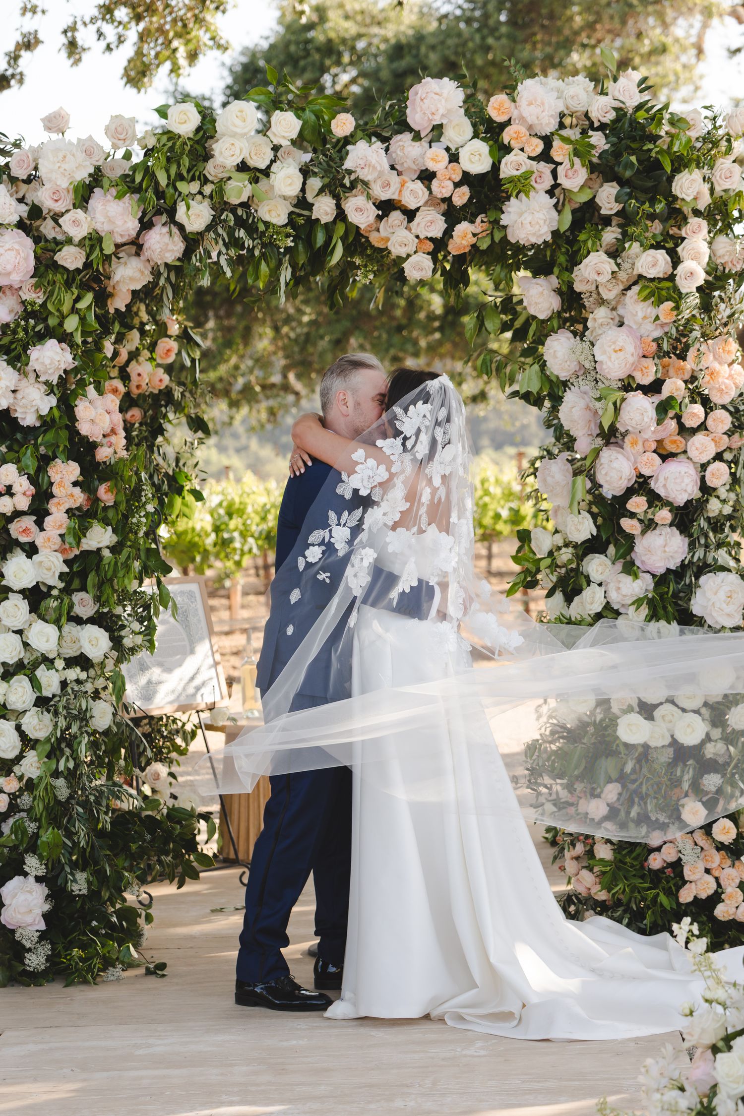 Wedding ceremony setting under a lush floral arch with white and blush roses.