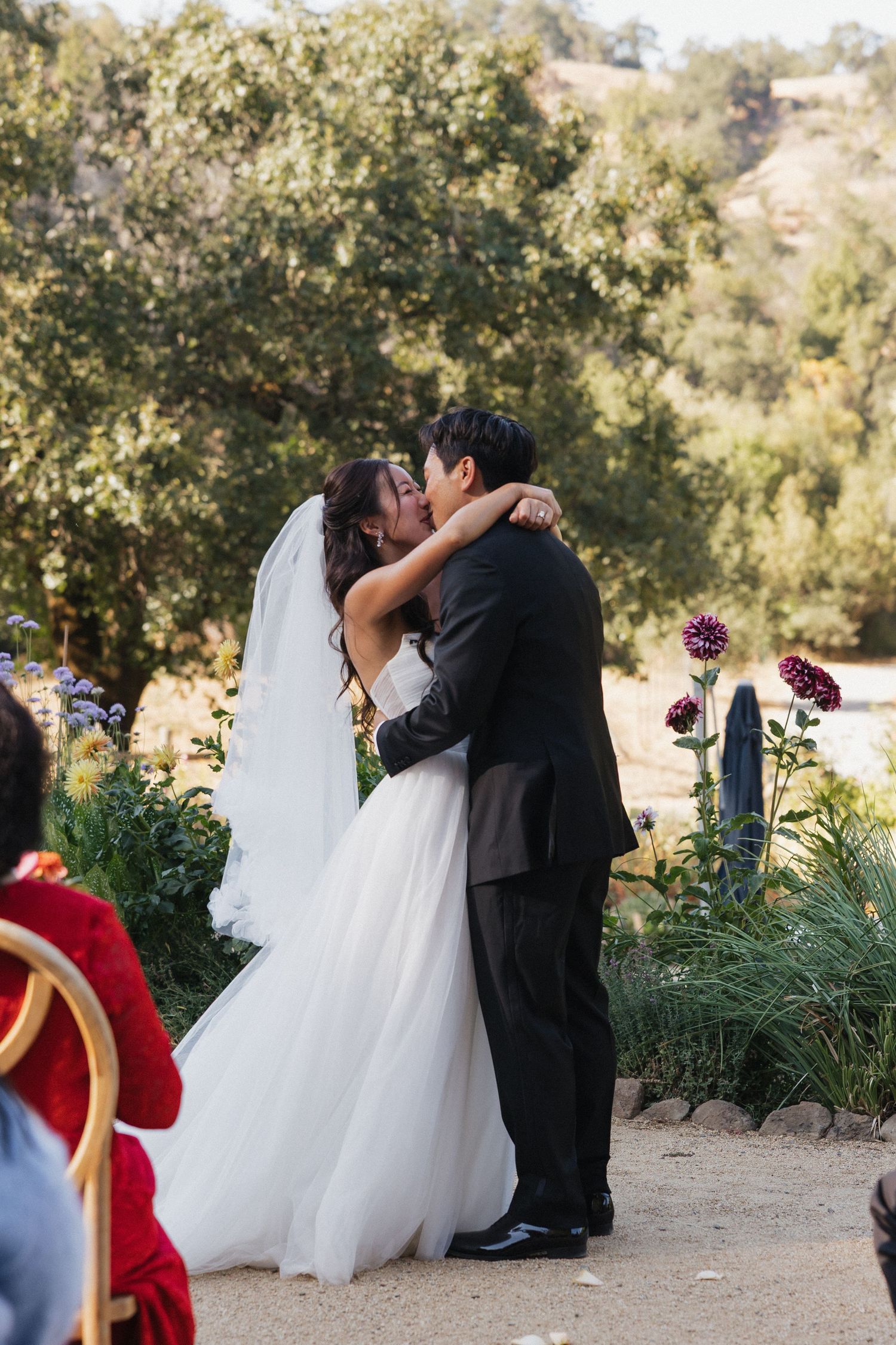 Newlyweds share their first kiss during an outdoor garden wedding ceremony.