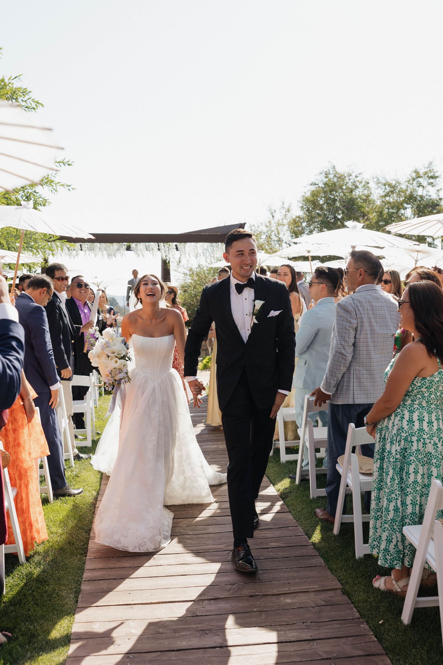 Wedding guests line a wooden walkway as the newlyweds make their exit after the ceremony.
