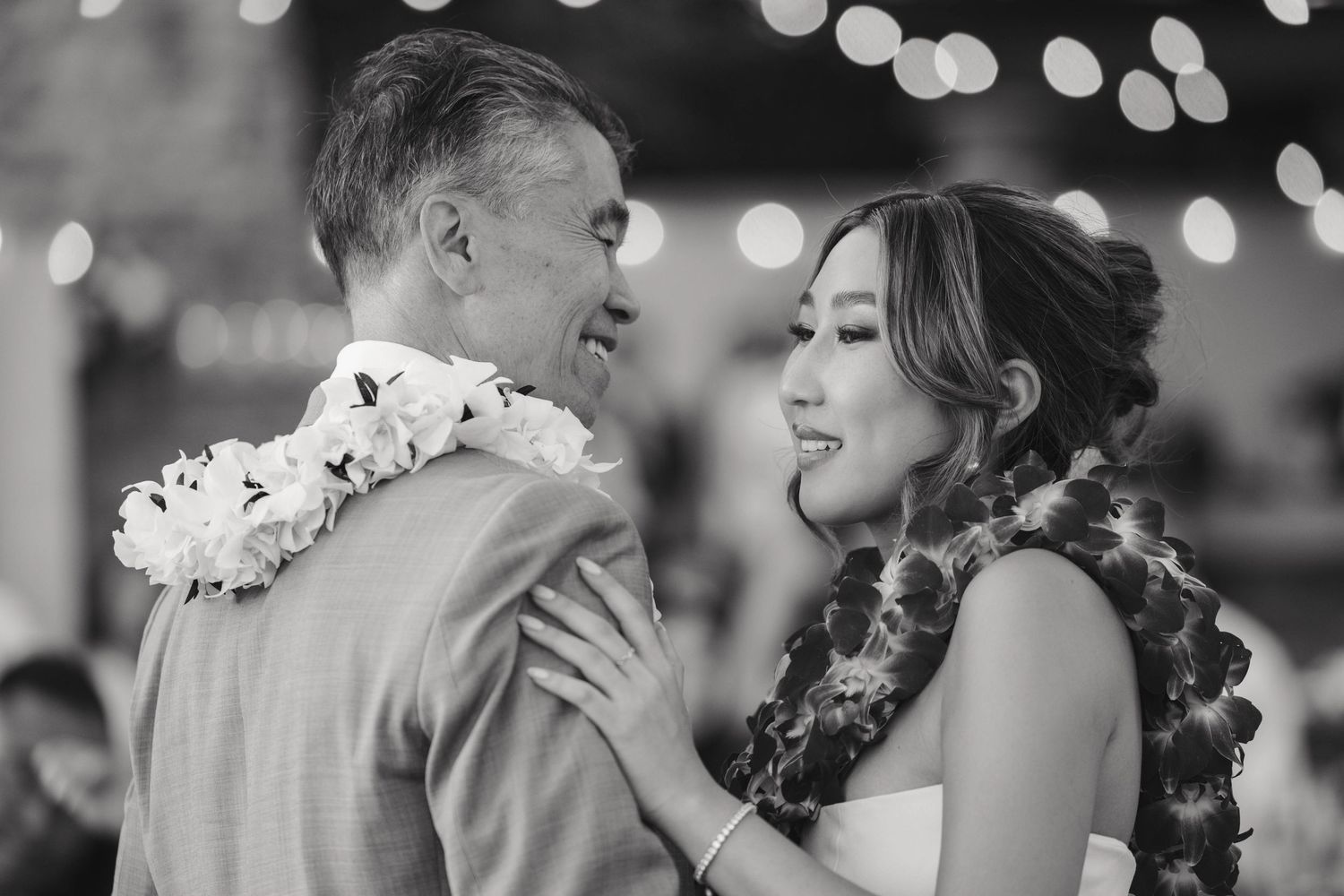 Candid black and white wedding photo showing bride and wedding party sharing joyful laughter during outdoor celebration.