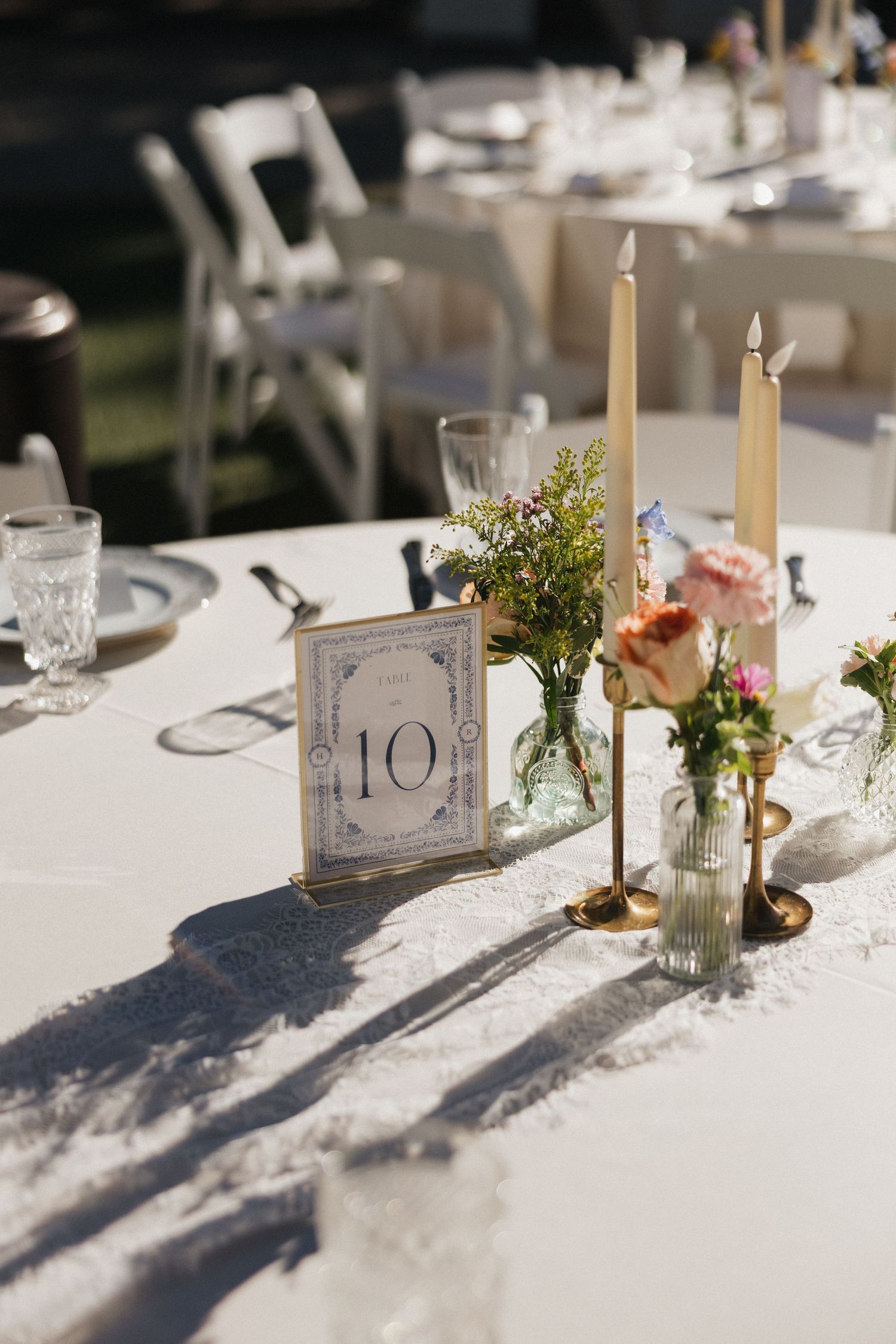 Elegant wedding reception table settings with white linens, candles, and small floral centerpieces.