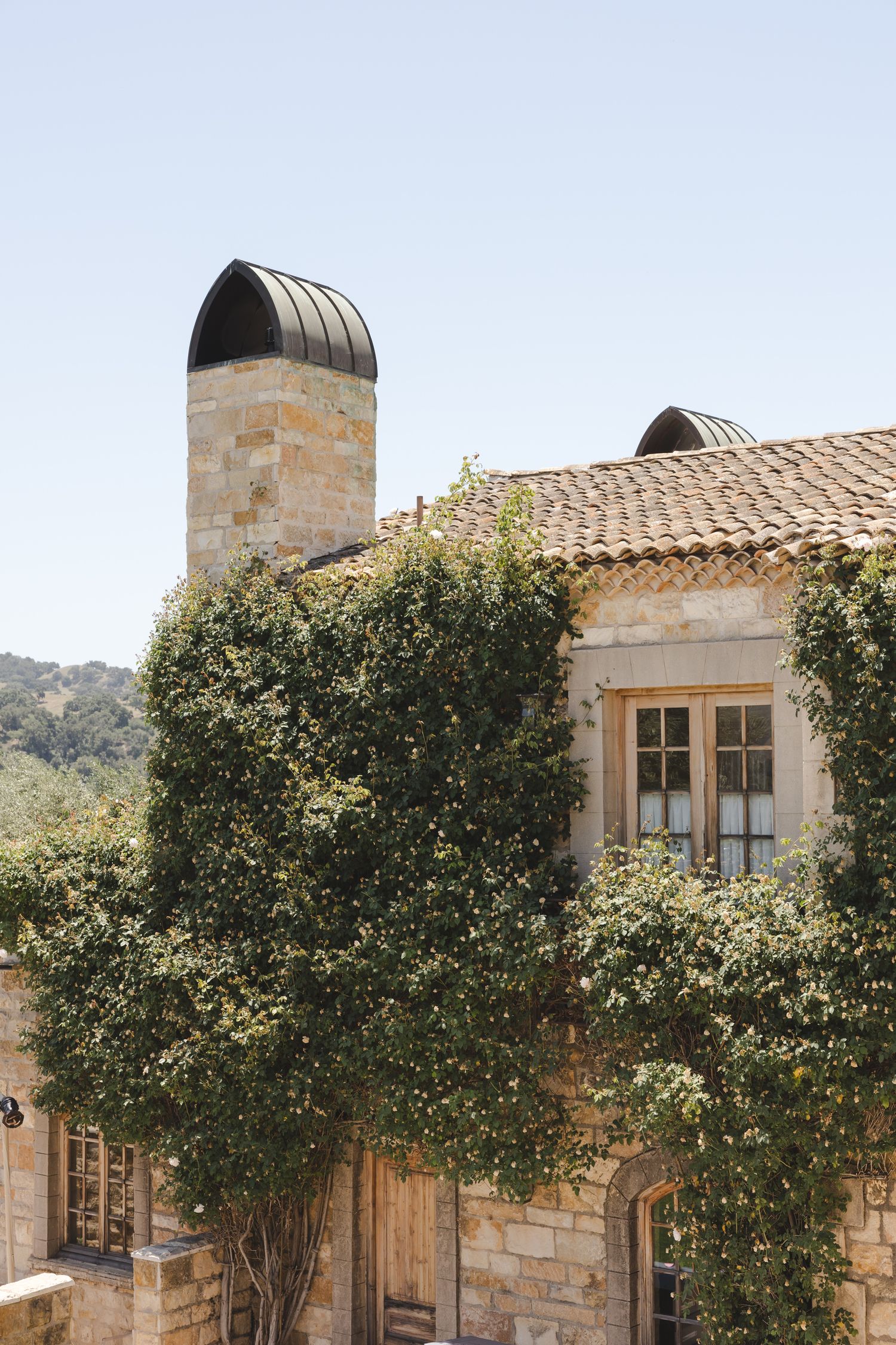 Stone facade of a Mediterranean-style villa with terracotta roof tiles and climbing greenery.