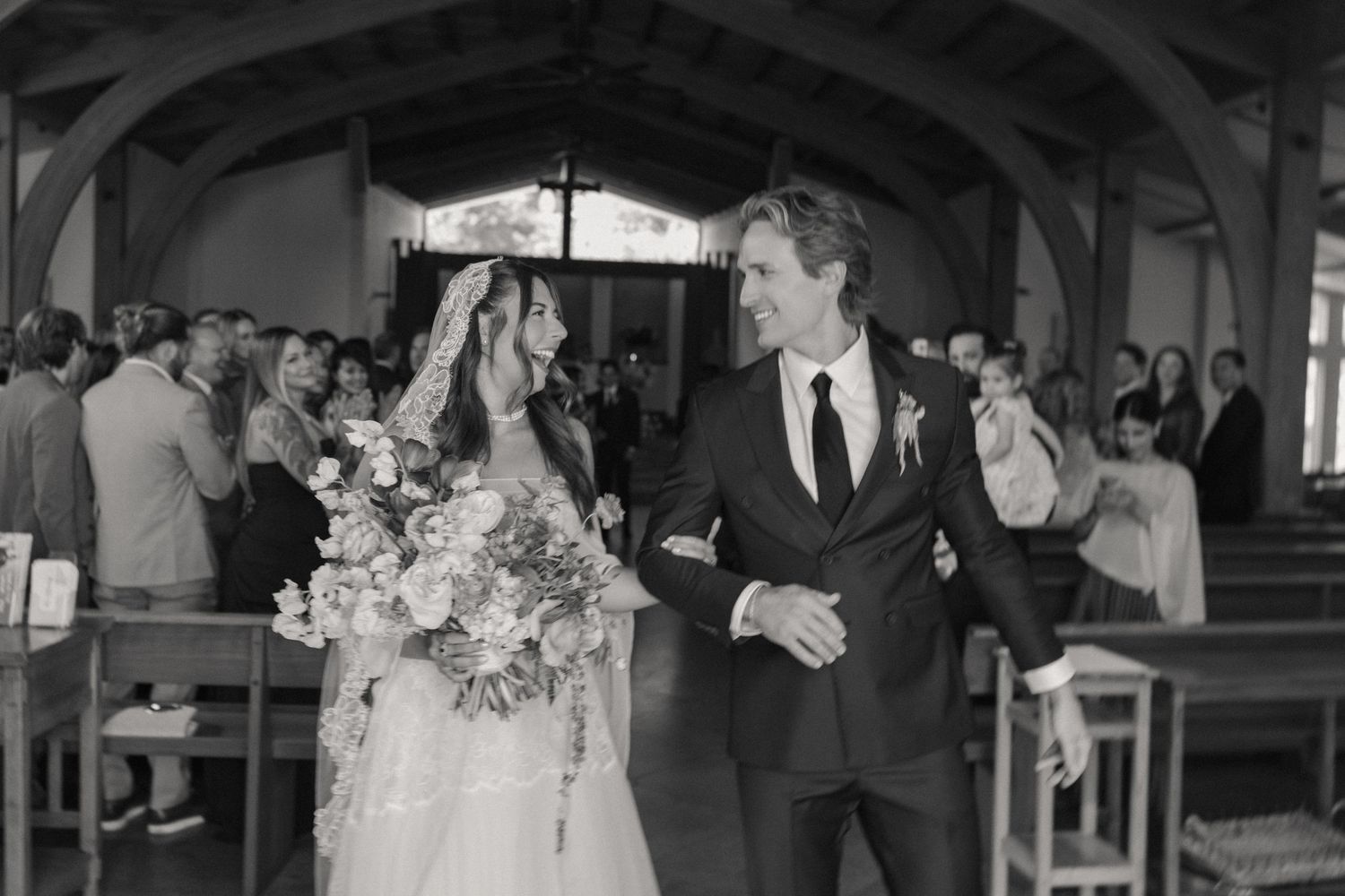 Bride and groom walk down church aisle after wedding ceremony in black and white photo.