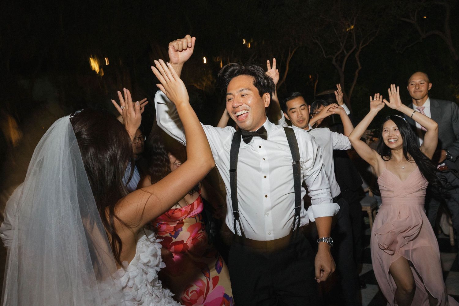 Wedding guests dancing and celebrating at a lively nighttime reception.