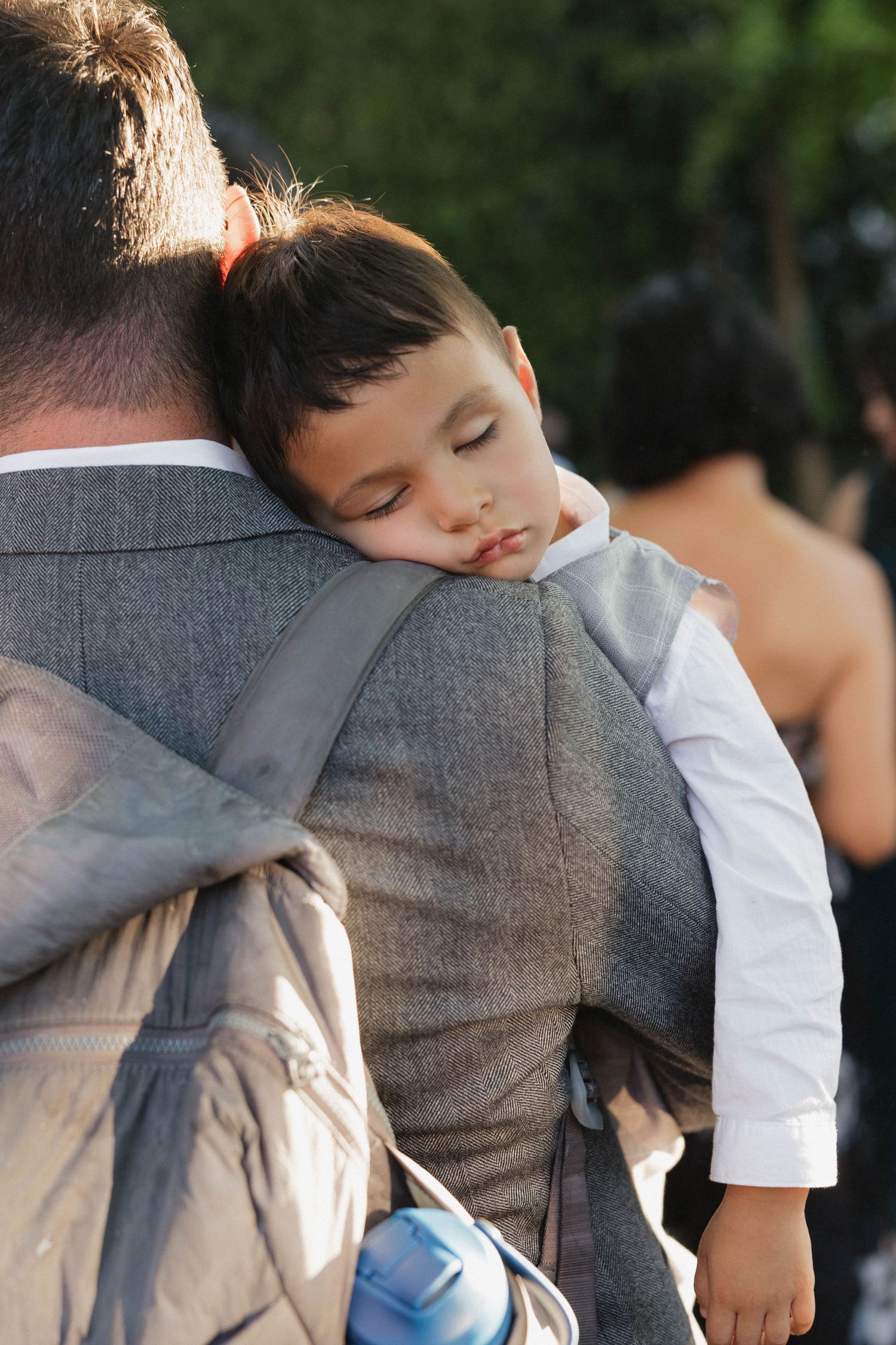 A small child in formal wear sleeps peacefully on someone's shoulder at an event.