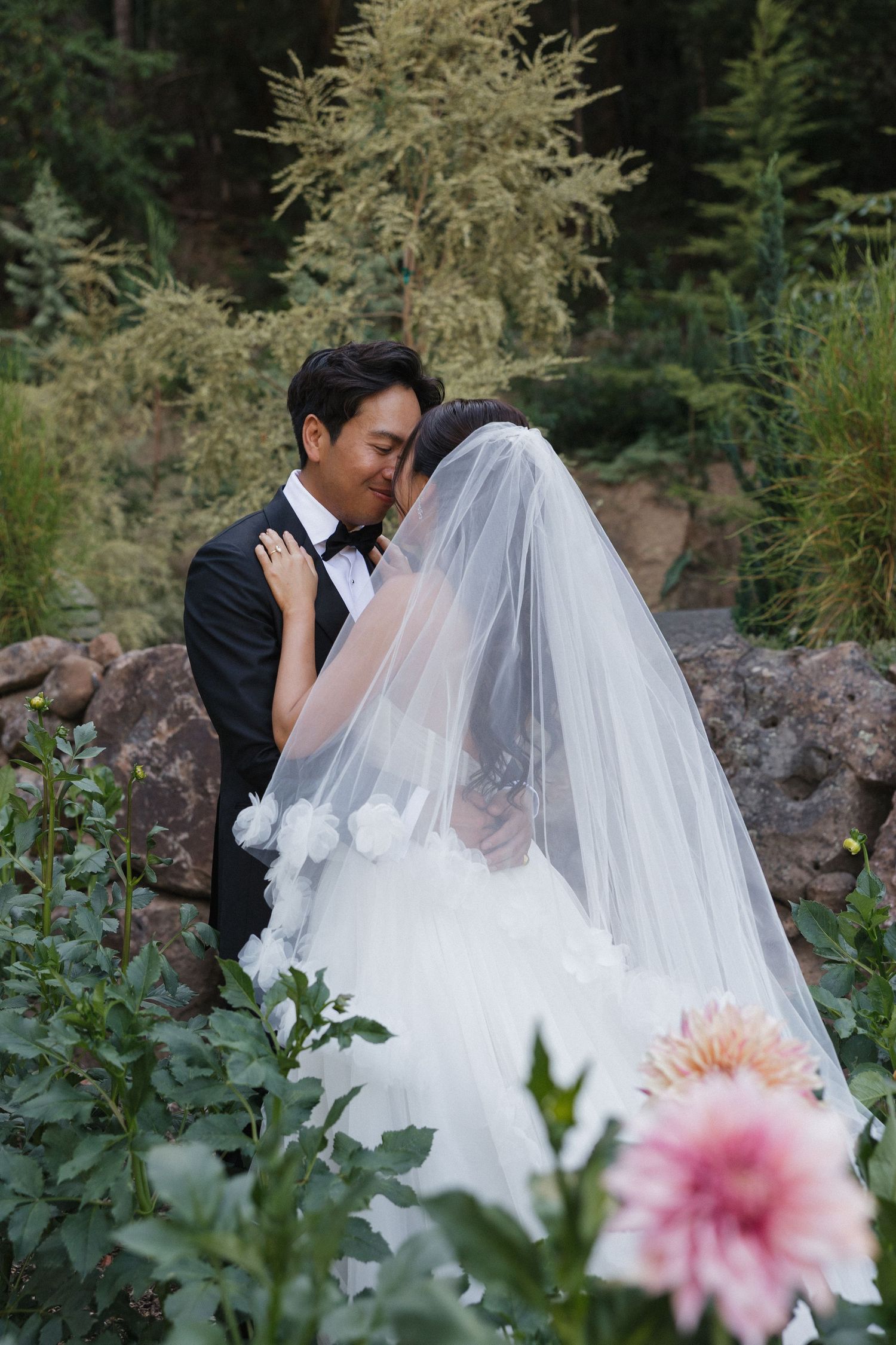 A romantic wedding photo captured in a garden with blooming dahlias in the foreground.