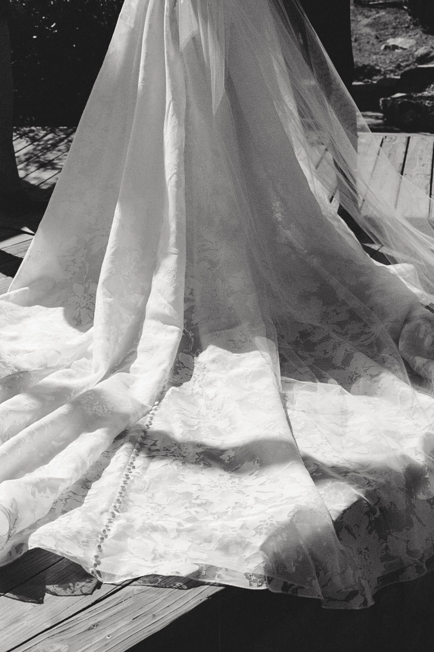 Black and white close-up photo of a wedding dress train with delicate lace details sprawled across wooden floor.