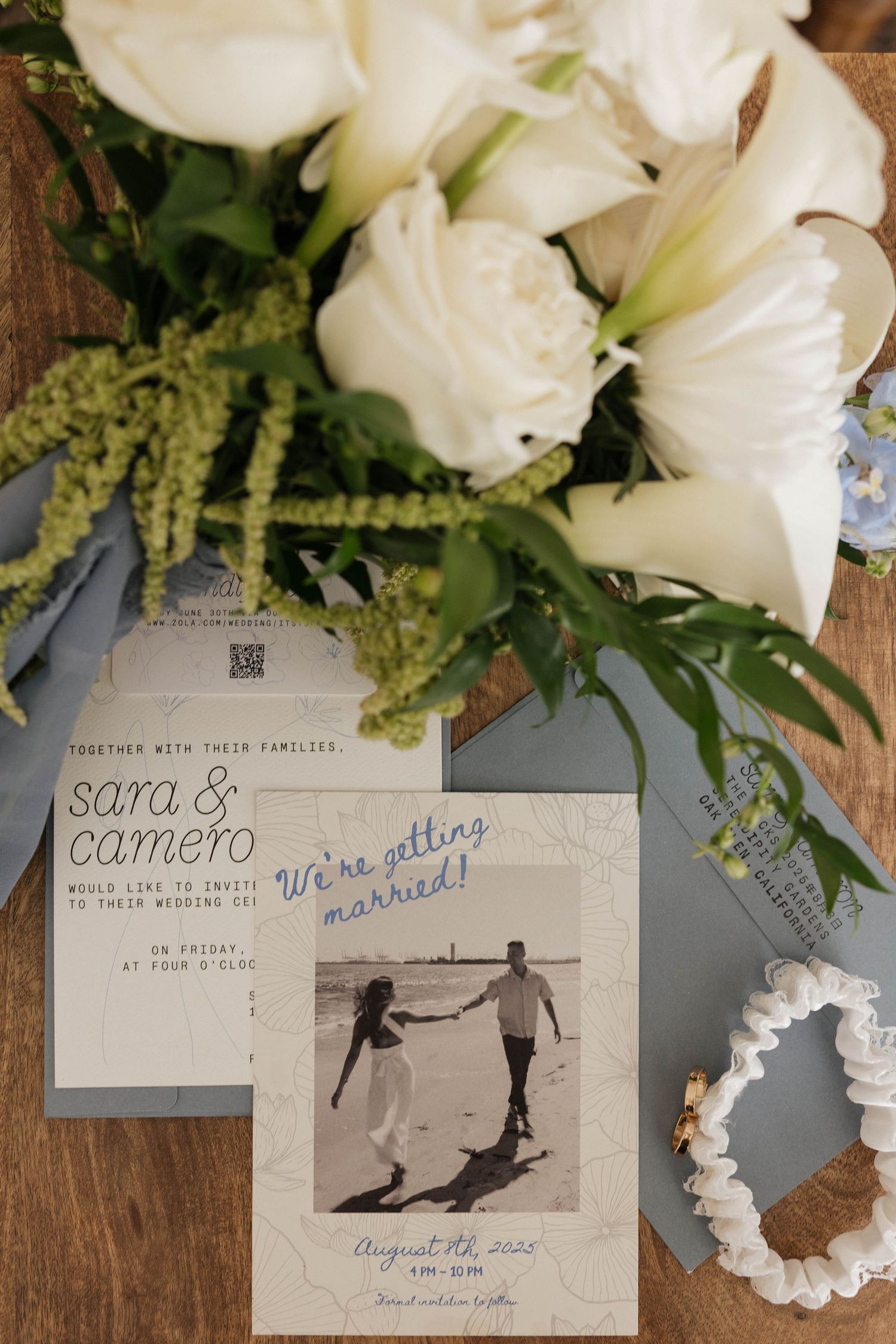Wedding invitation suite with white flowers and vintage photographs on wooden surface.